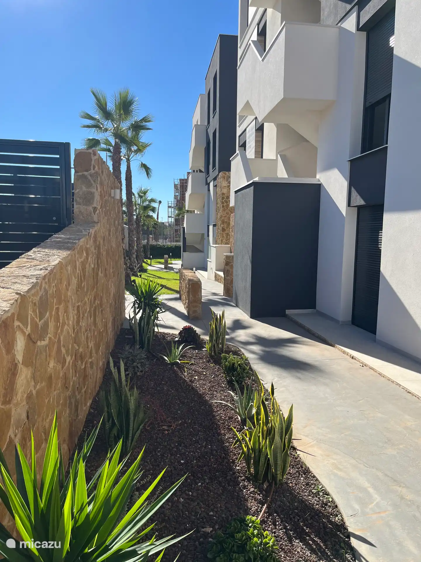 Puerta de entrada de la manzana 6/7/8 con un jardín bellamente ajardinado, rodeada de senderos bien cuidados con palmeras y vegetación.