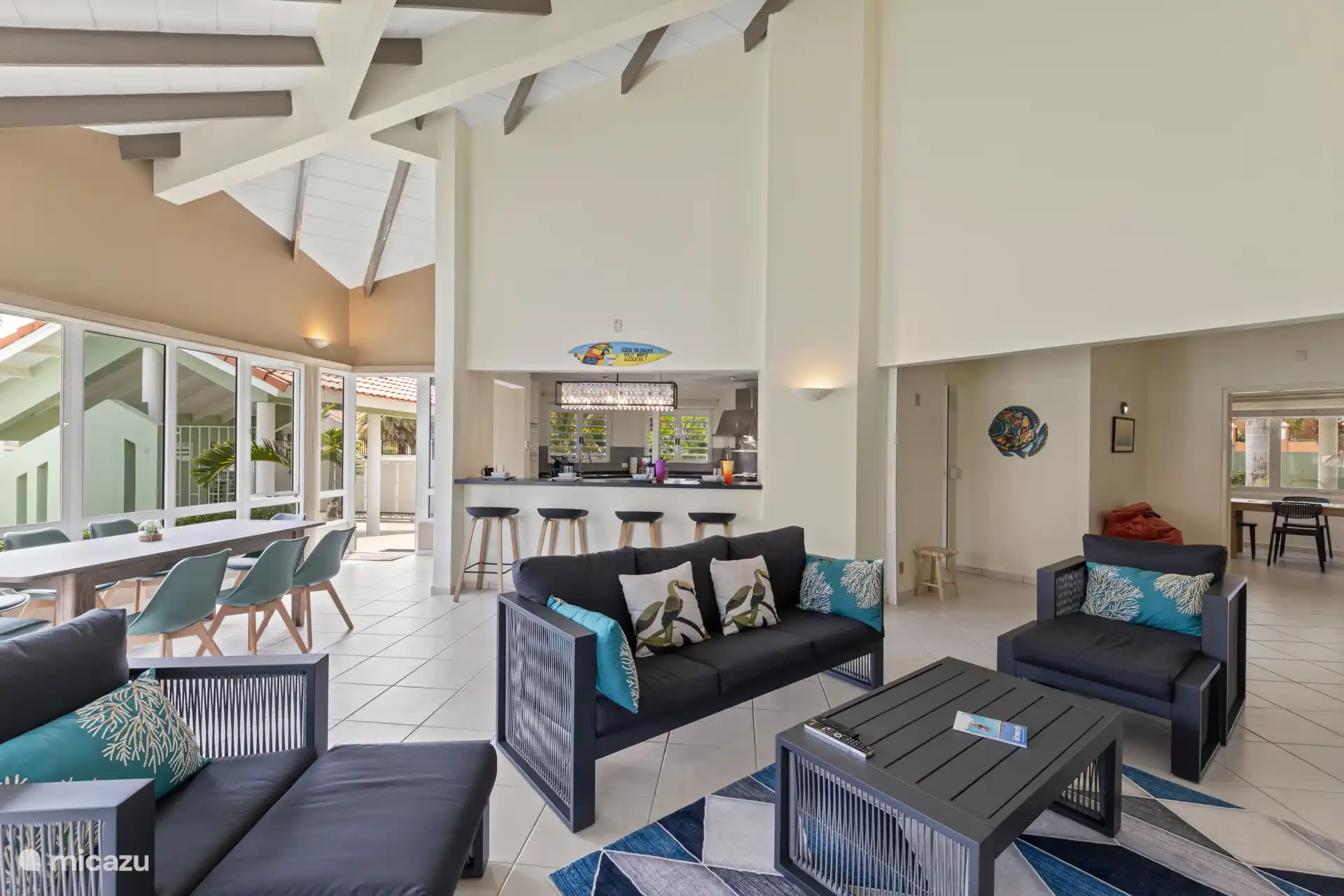 Ruime open woonruimte met bar, schommelstoel en een glazen gevel die het zwembad en terras naar binnen brengt.