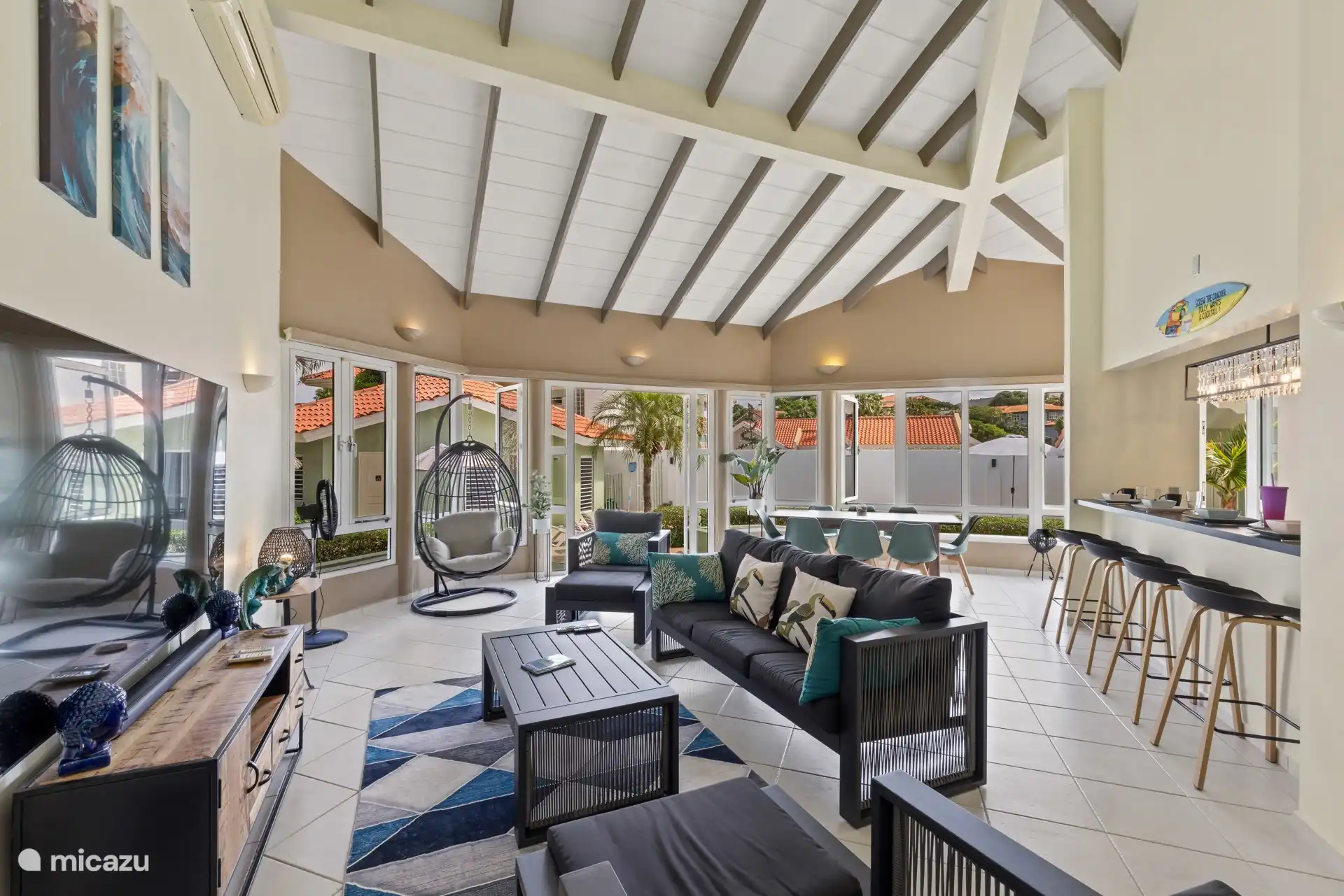 Ruime woonkamer met hoge plafonds, comfortabele zitplaatsen en uitzicht op de tuin door de ramen.