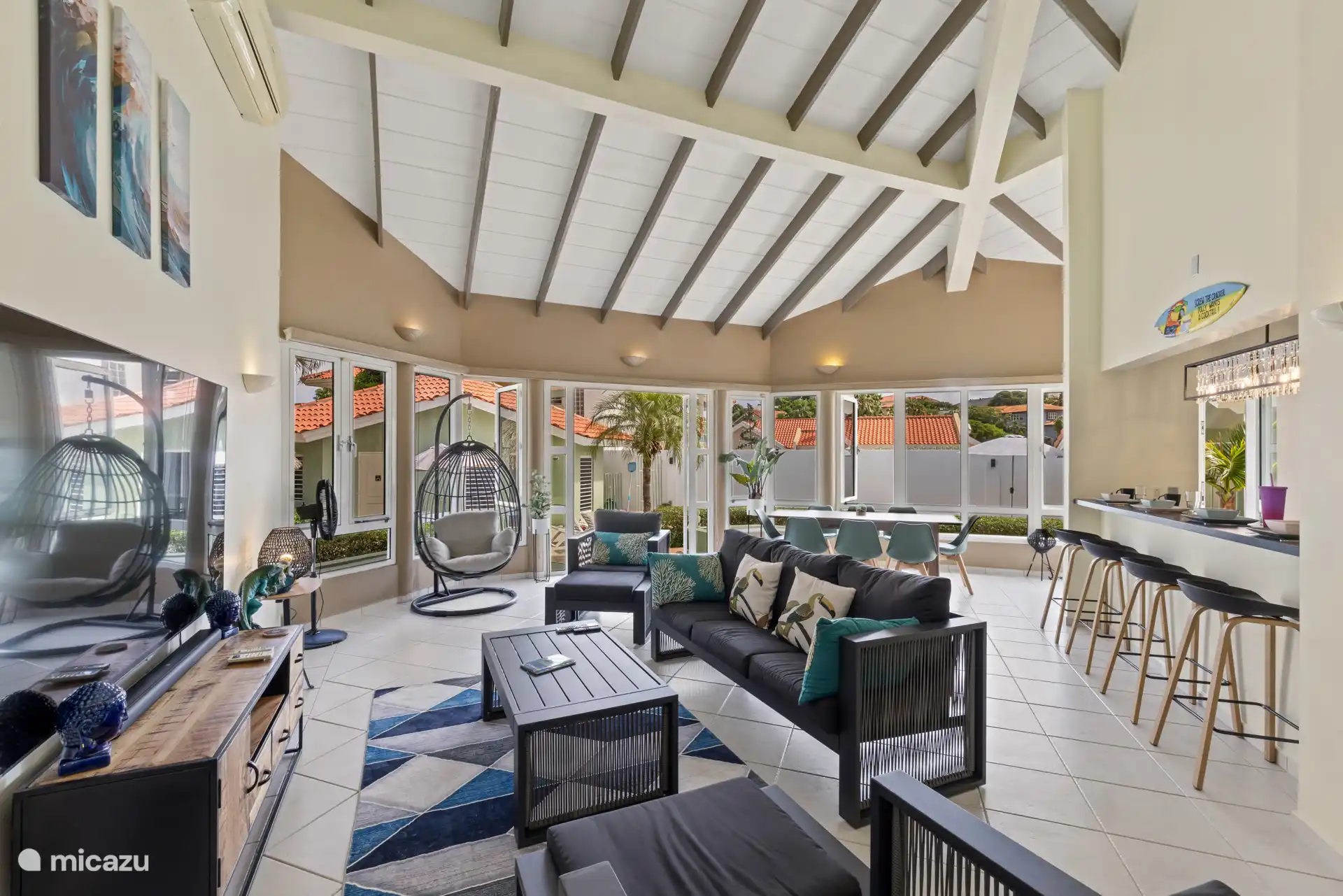 Ruime woonkamer met hoge plafonds, comfortabele zitplaatsen en uitzicht op de tuin door de ramen.