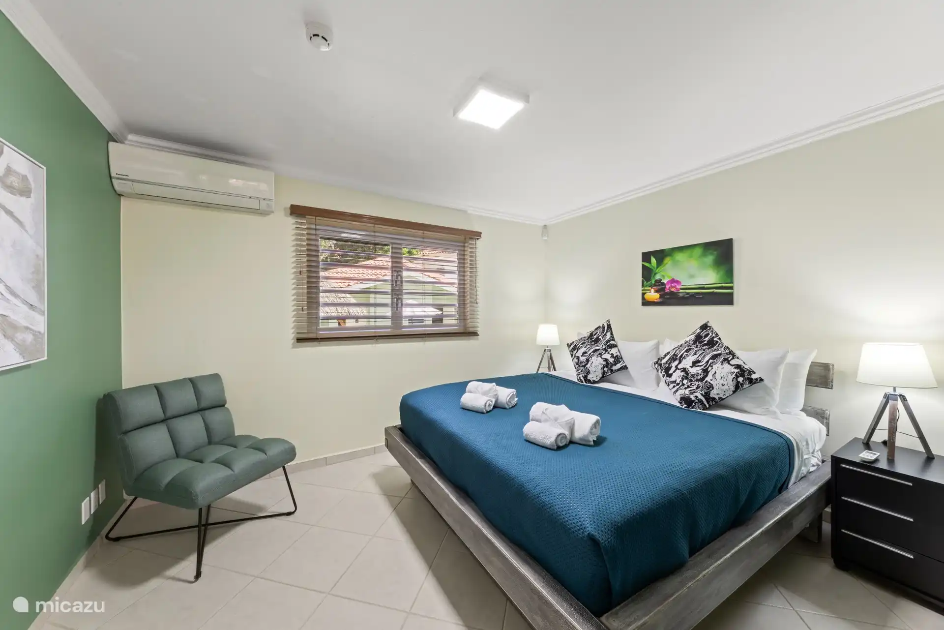 Een lichte kingsize slaapkamer met airco, uitzicht op de tuin en een ligstoel – een rustige plek om te ontspannen tussen eilandavonturen door.