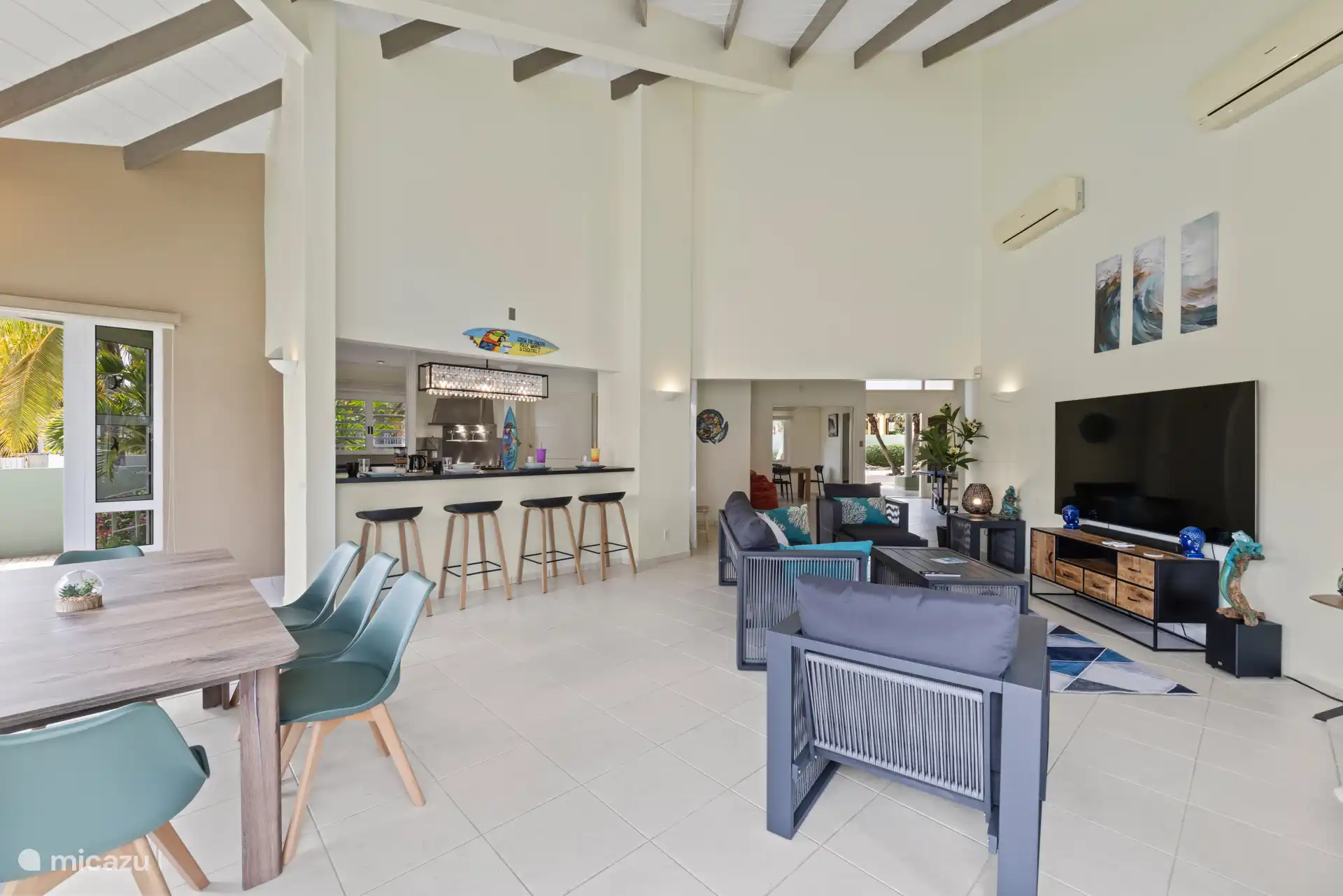 Ruime open woonruimte met bar, schommelstoel en een glazen gevel die het zwembad en terras naar binnen brengt.