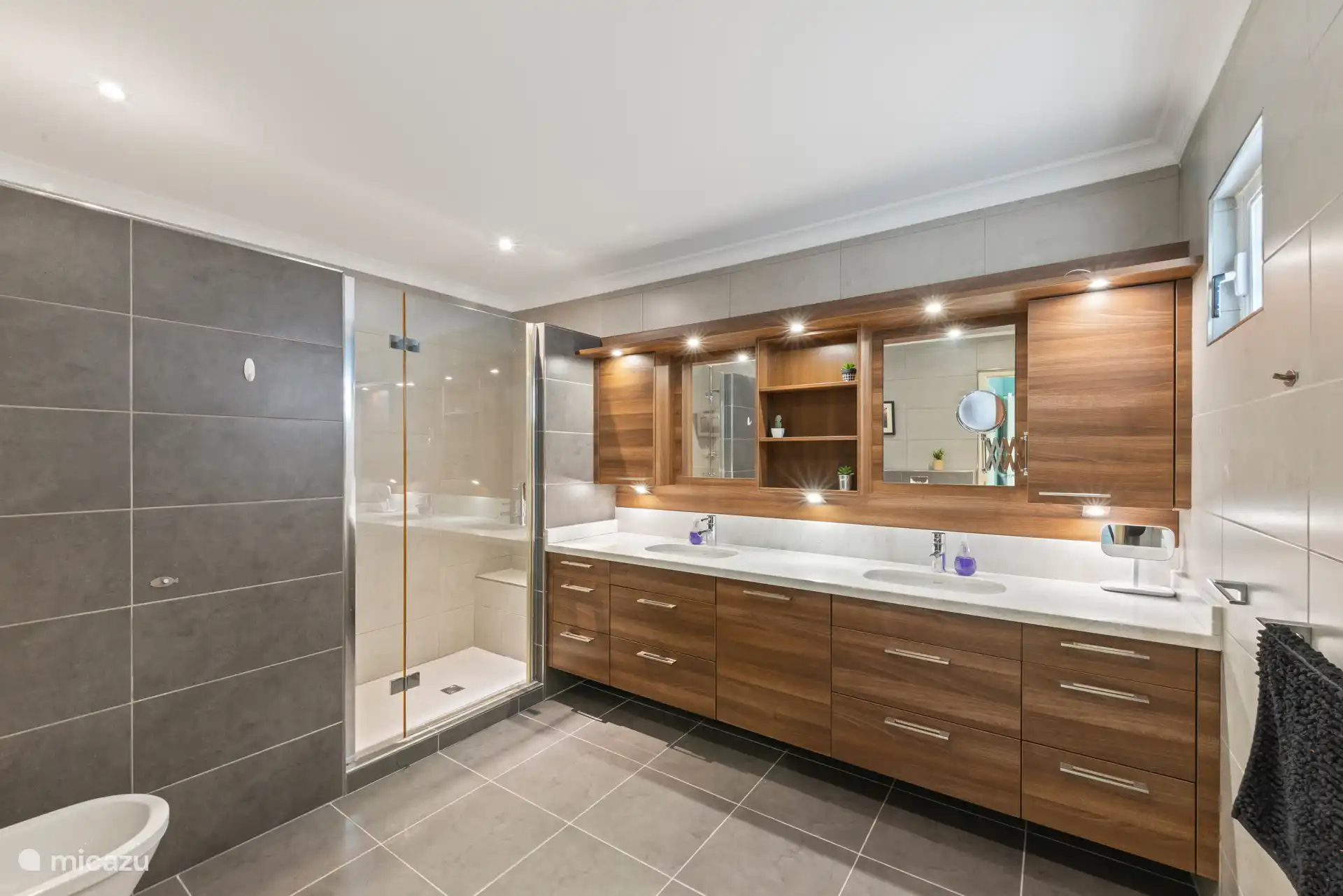 Ruime hoofdbadkamer met dubbele wastafels, grote spiegels en warme houten kasten