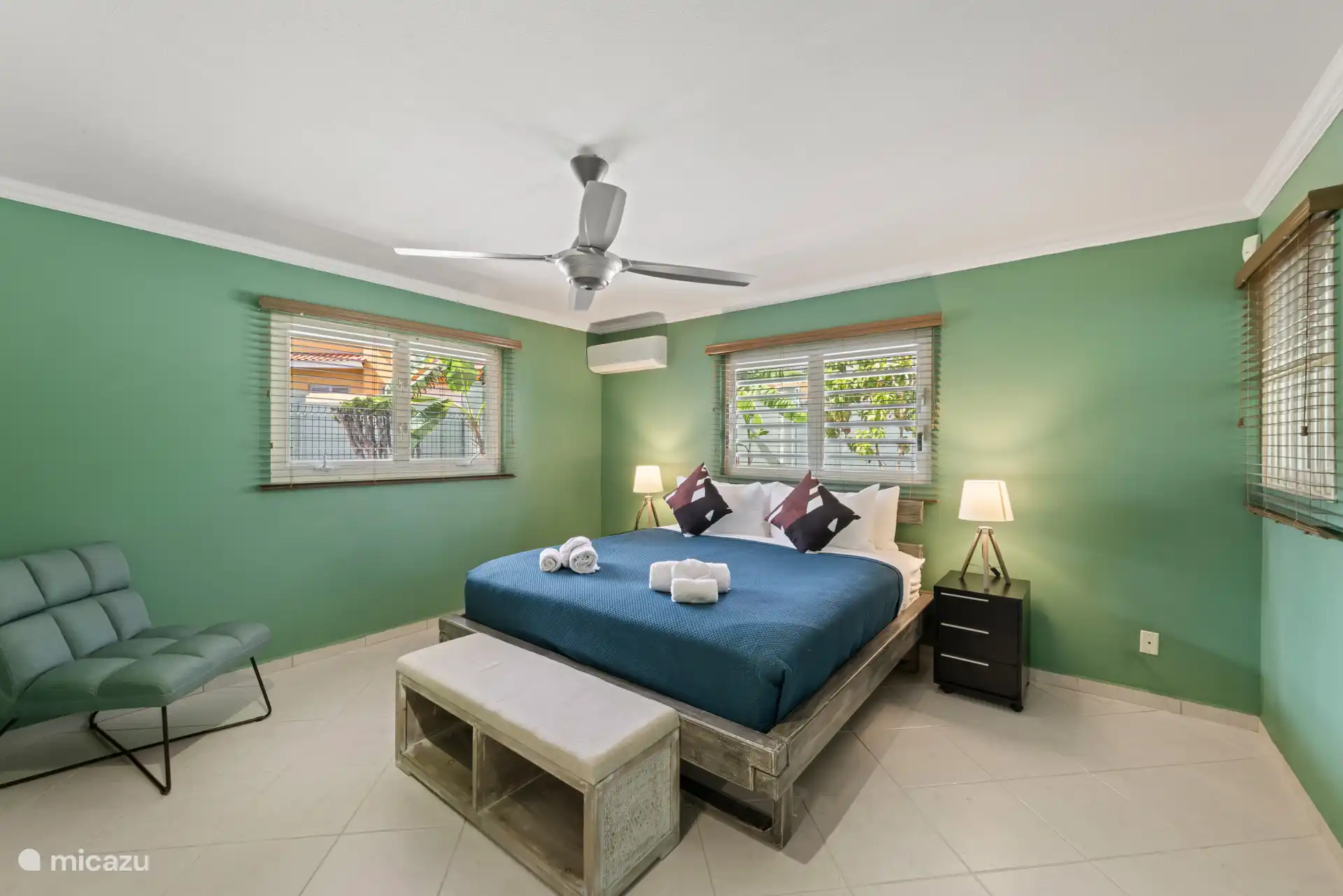 Ruime hoofdslaapkamer met een comfortabele kingsize bed en grote ramen die de kamer vullen met natuurlijk licht – jouw rustige plek om op te laden na een dag in de zon.