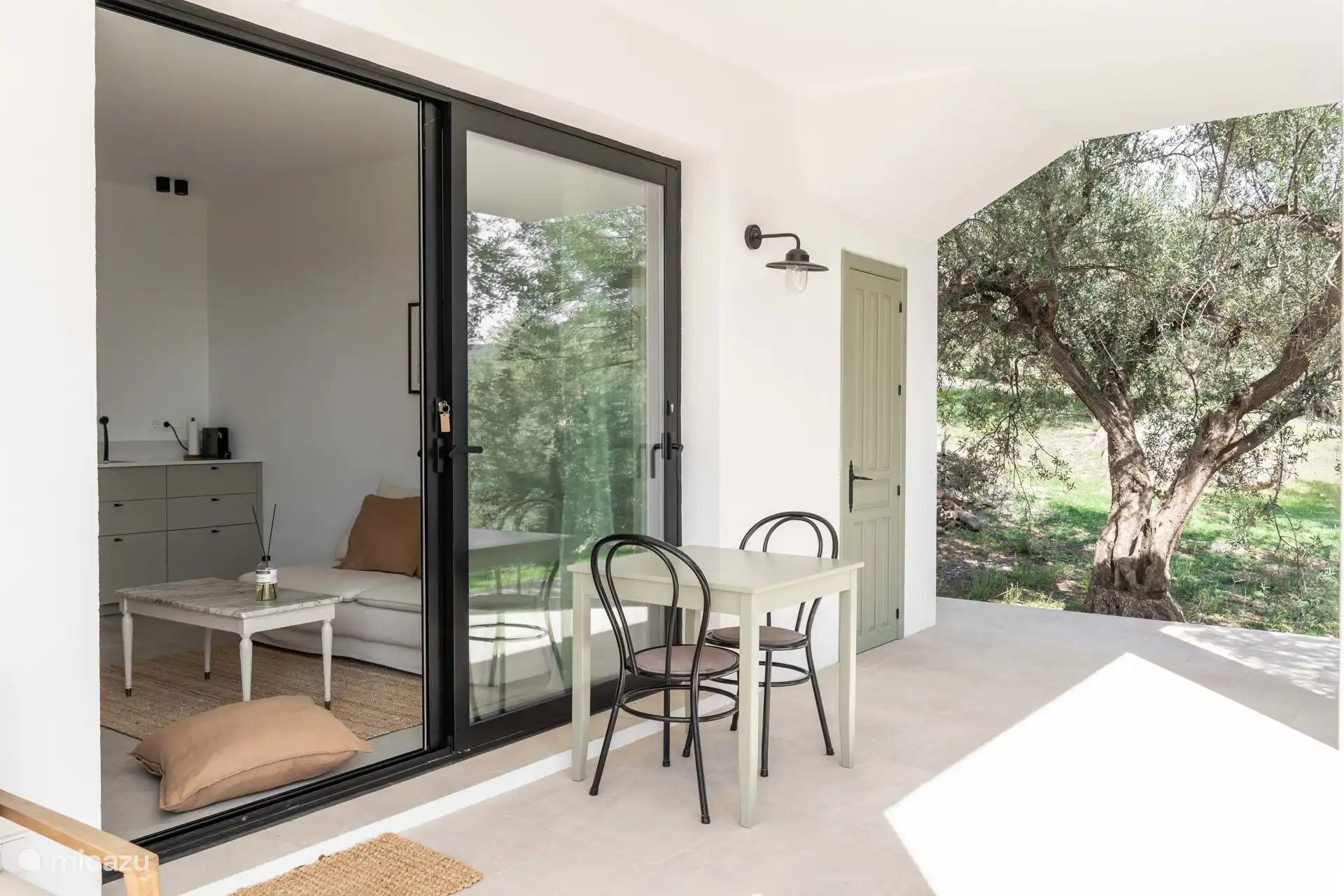 De kleinere woonkamer heeft een schuifdeur die uitkomt op de veranda. Door de bomen rondom heb je hier genoeg schaduw.