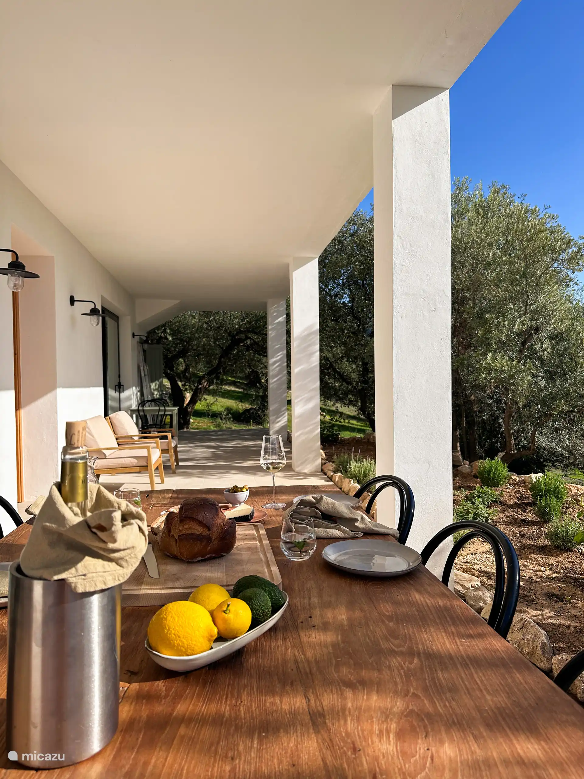 Aan de voorzijde van het huis zit een lange veranda waar een grote eettafel staat. De perfecte plek om 's ochtends in de zon te ontbijten of een borrel te drinken