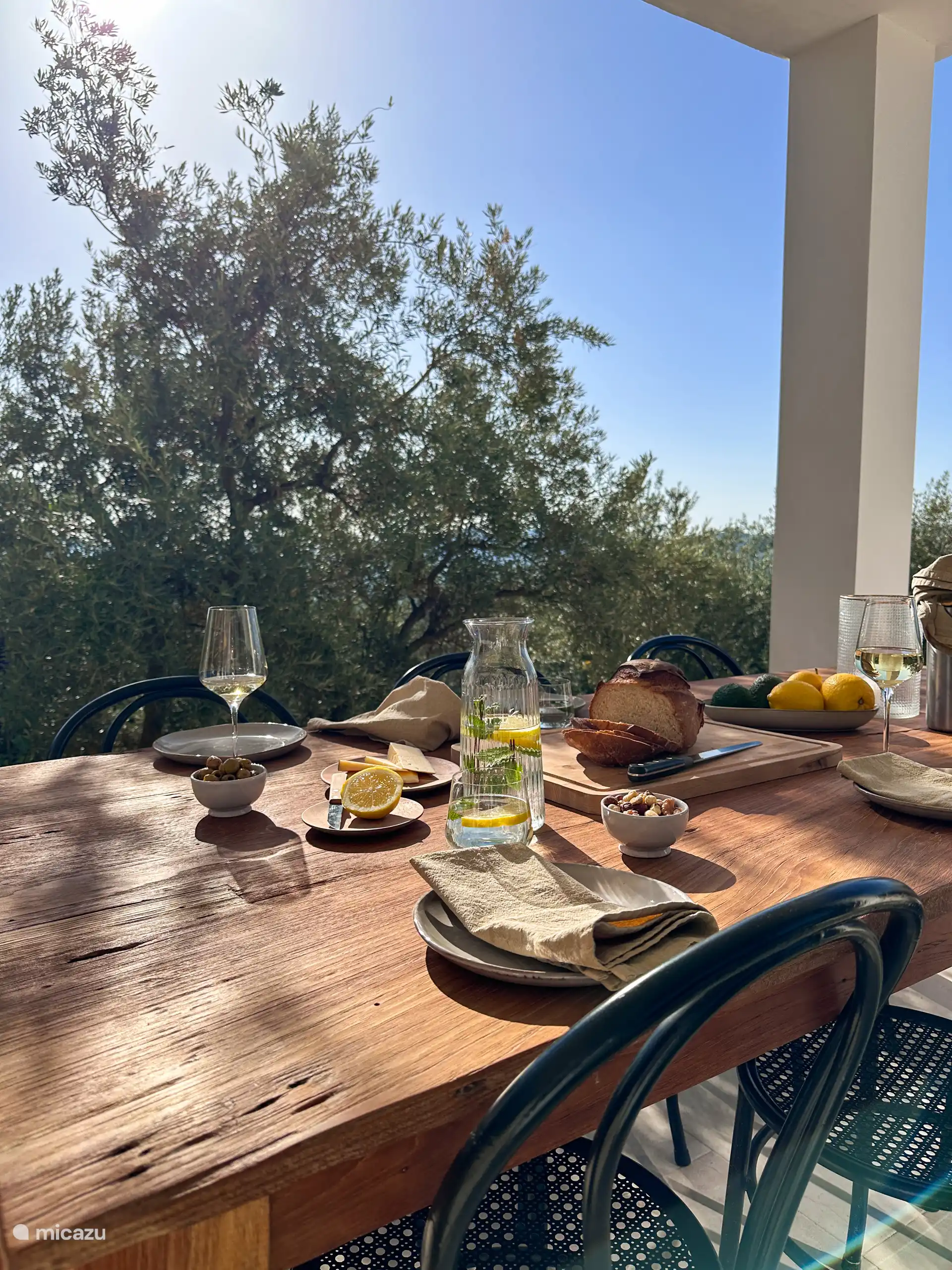 Aan de voorzijde van het huis zit een lange veranda waar een grote eettafel staat. De perfecte plek om 's ochtends in de zon te ontbijten of een borrel te drinken