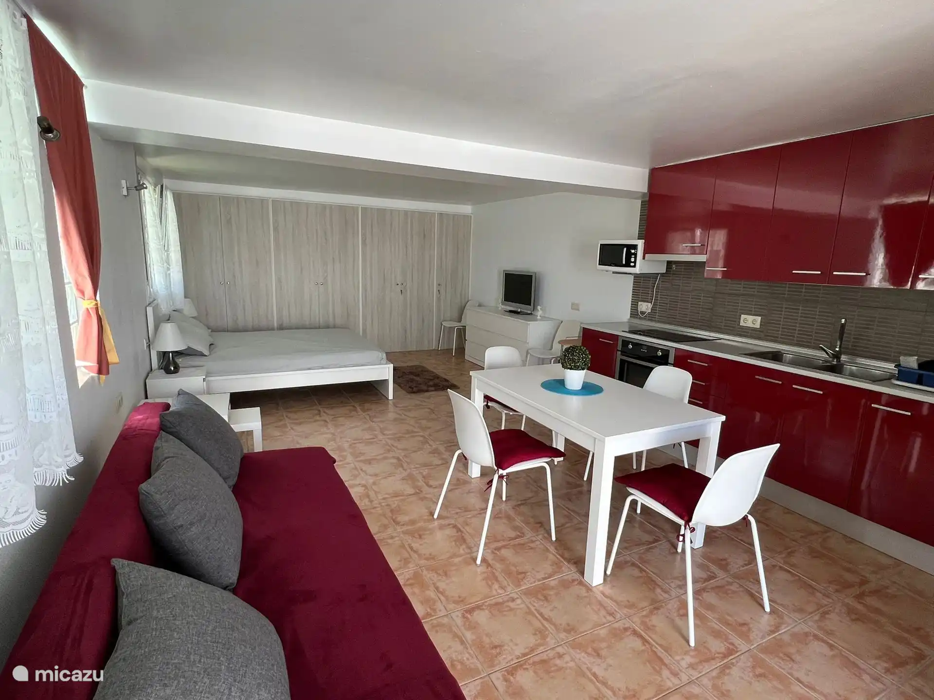 Zijaanzicht van de keuken, de tafel in de woonkamer met de stoelen, de bank en het bed van het loftappartement