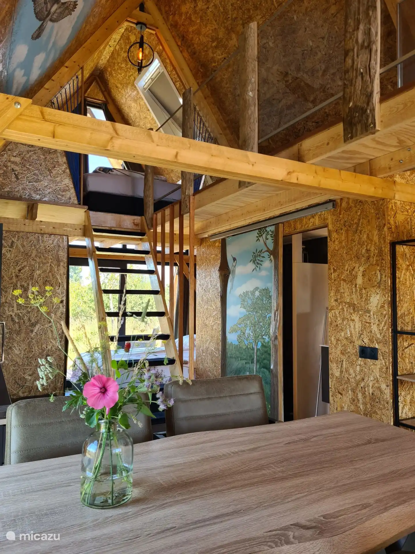 half hoge tafel met dito stoelen en zicht op het slaapzoldertje met 2 losse bedden