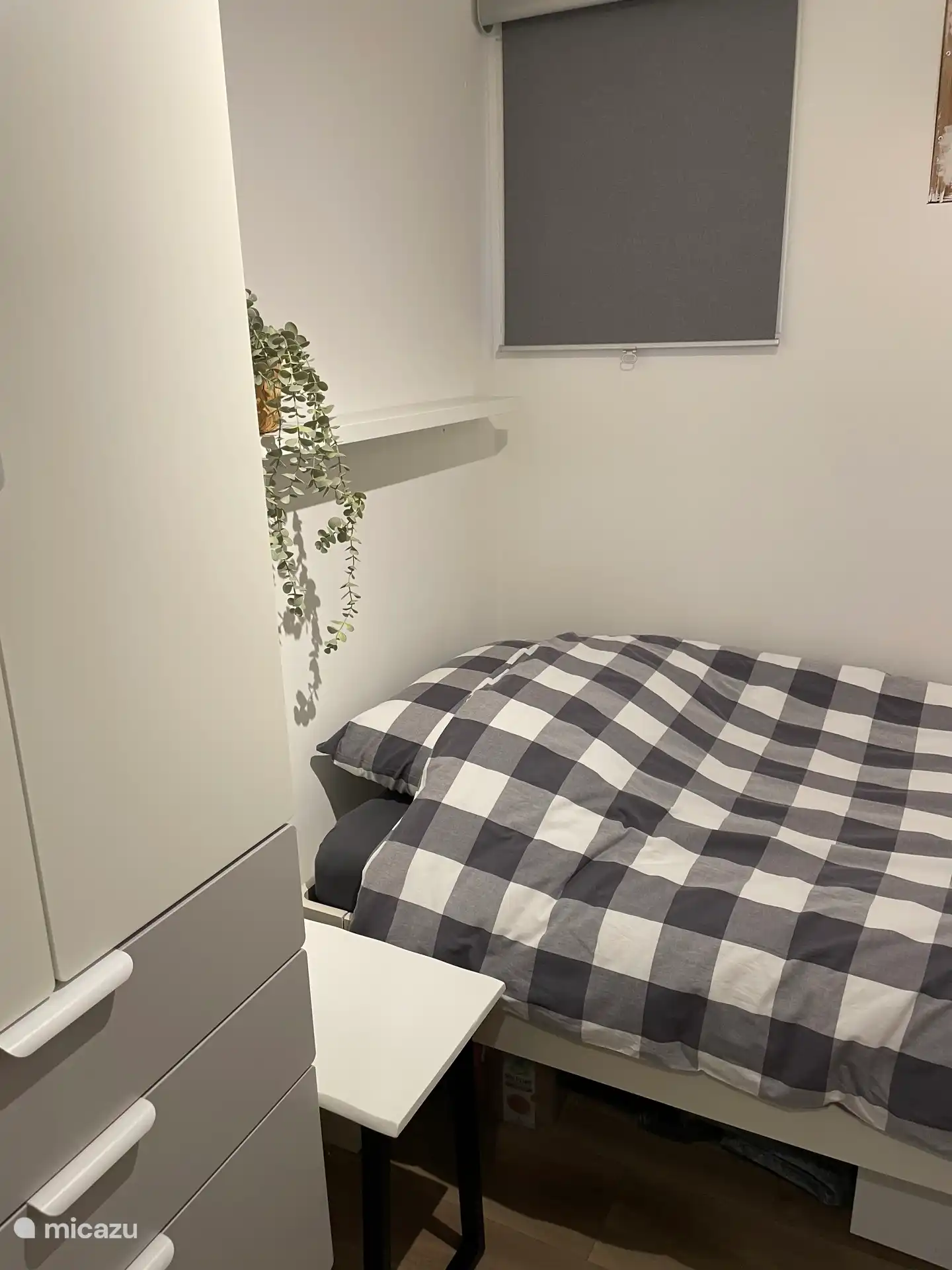 Habitación para una persona con cama alta de Auping. Armario alto, mesilla de noche con lámpara y silla extra.
