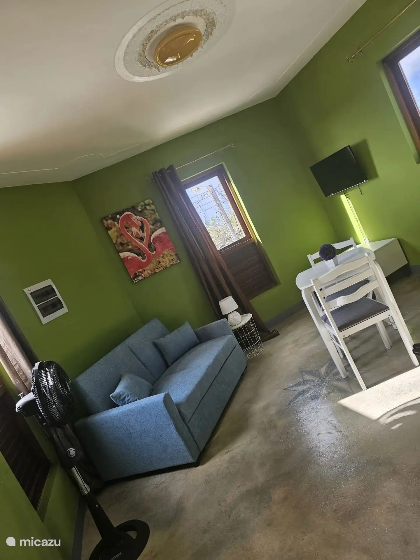 Espace salon avec 2 personnes. canapé, table à manger avec chaises et télévision avec chaînes internationales, il y a également un ventilateur.