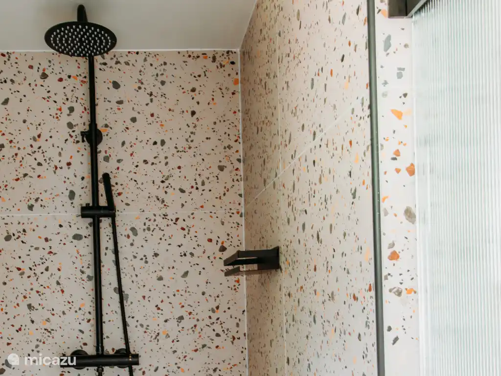 De badkamer is voorzien van een moderne regendouche. 