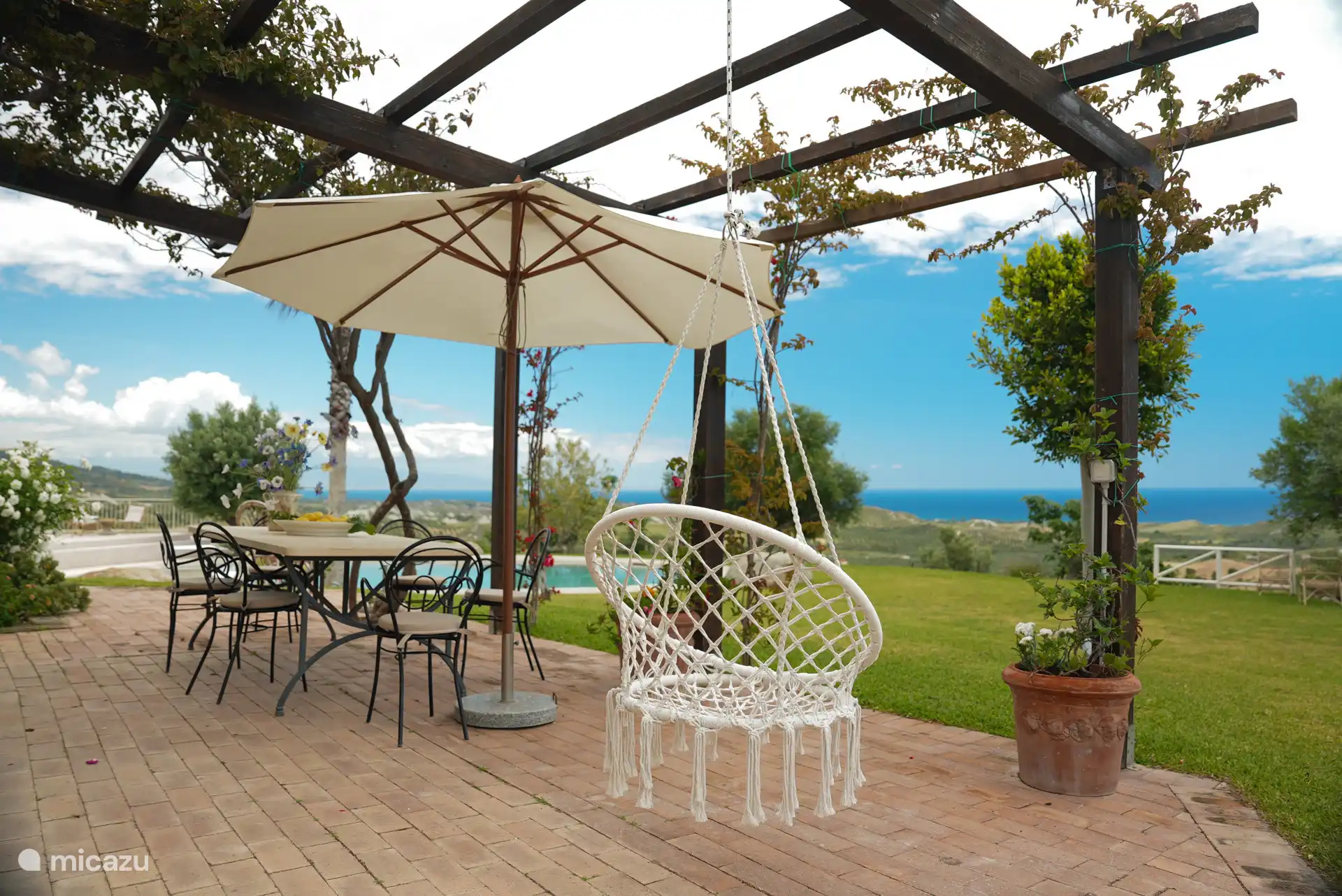 Ruim terras direct gelegen aan de keuken met eettafel, hangstoel en zicht op het zwembad en de zee. Hier komt het buitenleven van Villa Calabria mooi samen.