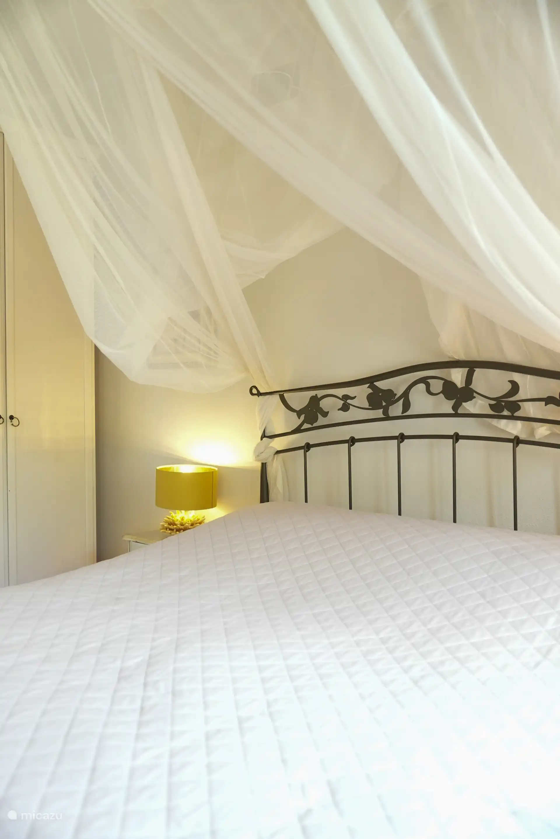Het bed in slaapkamer 1 heeft een rustige, romantische uitstraling met lichte stoffen en zachte verlichting. Een fijne plek om echt uit te rusten.