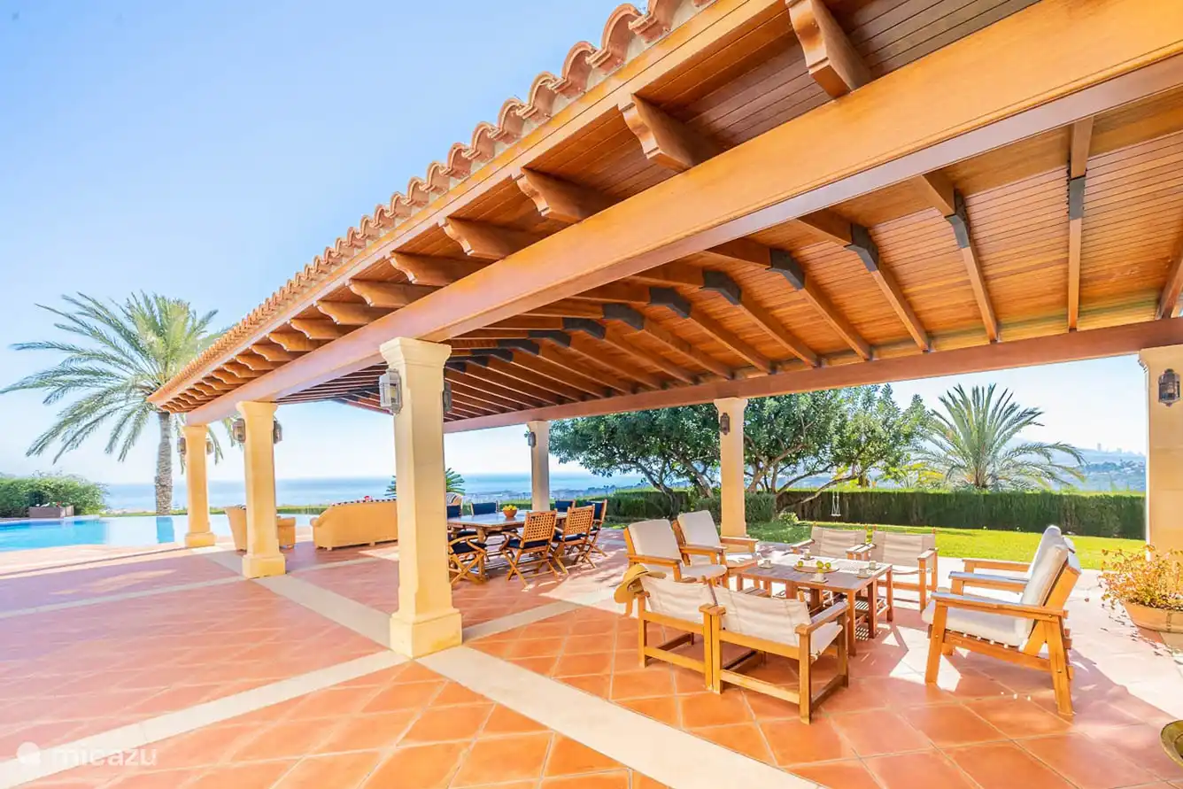 Salon extérieur sous la terrasse couverte, face à la piscine et la vue panoramique.