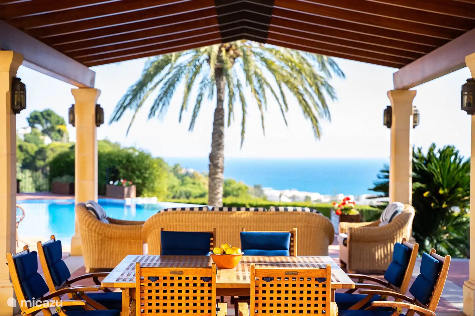 Salon extérieur sous la terrasse couverte, face à la piscine et la vue panoramique.