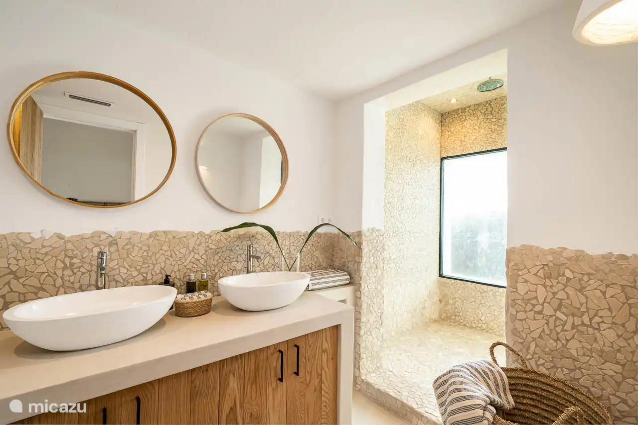 En-suite bathroom with shower, double sink, hairdryer, towels, products. 