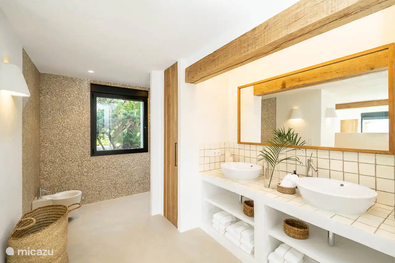 En-suite bathroom with shower, double sink, hairdryer, towels, products. 