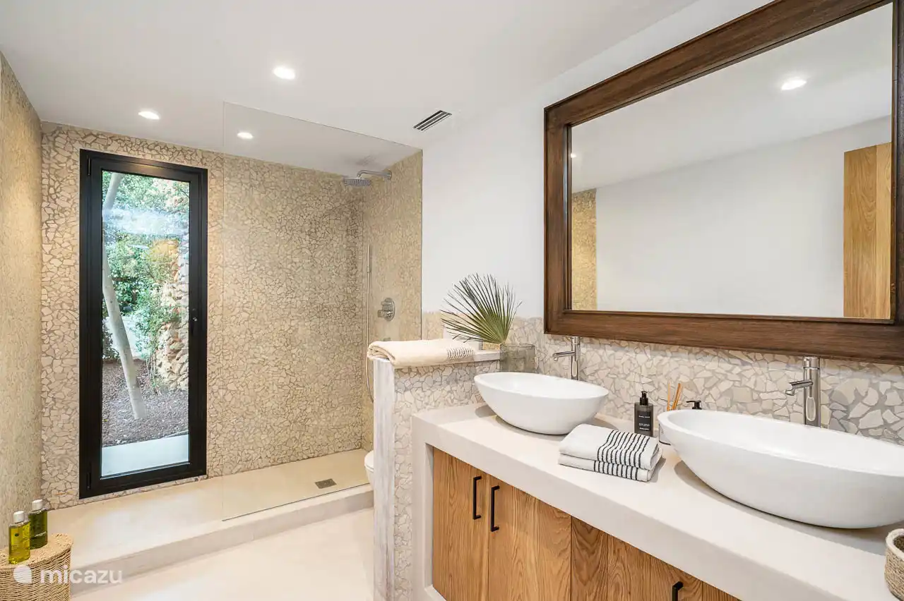 En-suite bathroom with shower, double sink, hairdryer, towels, products. 