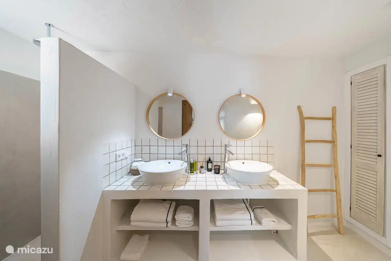 En-suite bathroom with shower, double sink, hairdryer, towels, products. 