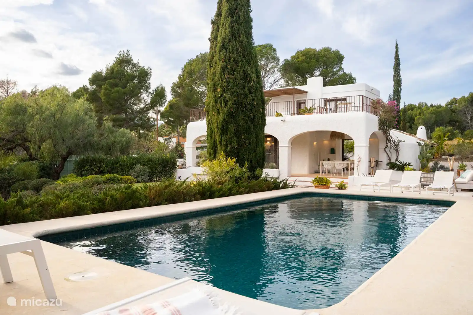 Swimming pool surrounded by a terrace with sun loungers, garden with trees, nature and mountain views, outdoor lounge.