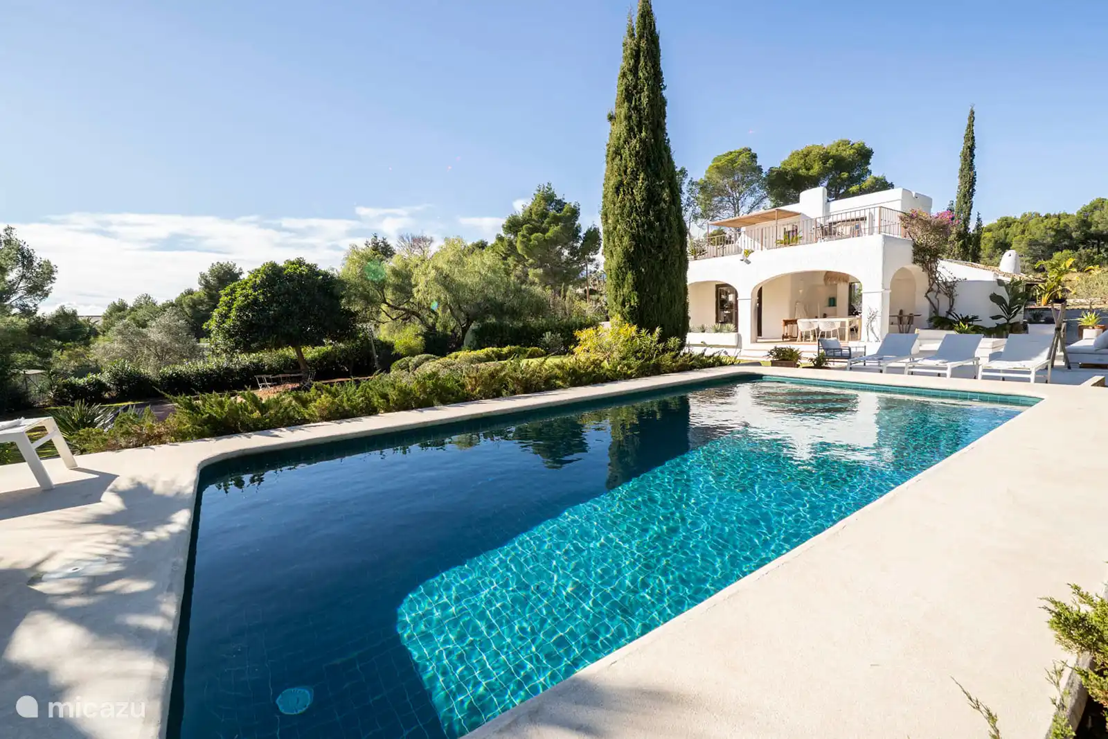 Swimming pool surrounded by a terrace with sun loungers, garden with trees, nature and mountain views, outdoor lounge.