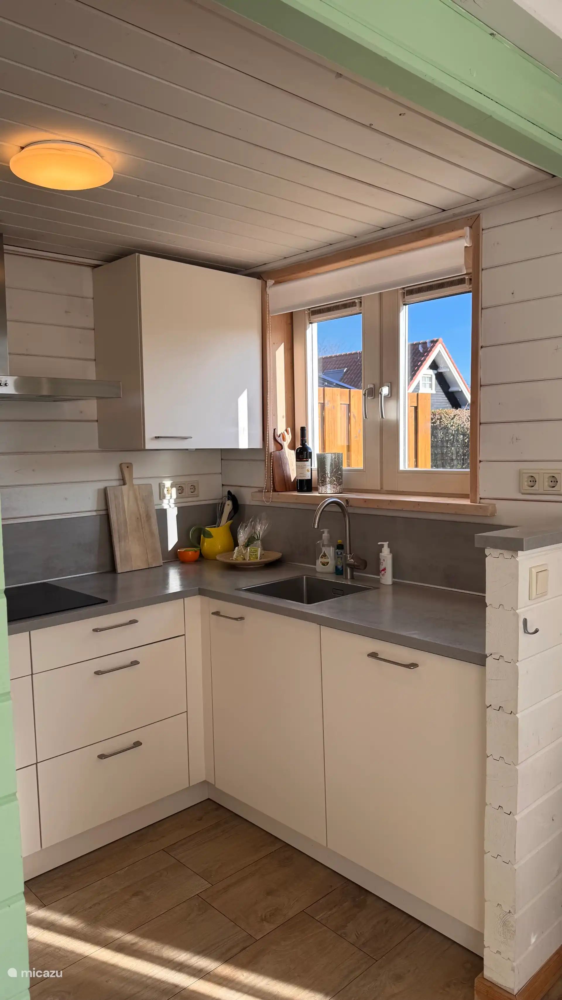 Gezellige keuken met lichte kleuren en natuurlijke accenten. Het daglicht door het raam en het uitzicht naar buiten zorgen voor een frisse, uitnodigende plek om samen te koken.