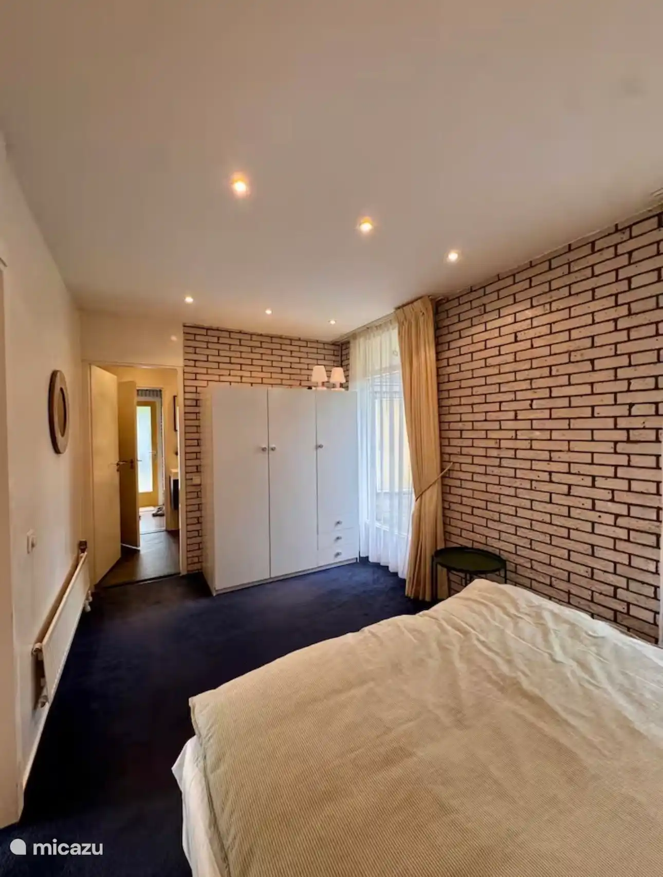 Ruime slaapkamer met veel licht en een warme bakstenen muur. De rustige kleuren en comfortabele inrichting zorgen voor een ontspannen en fijne plek om te overnachten.