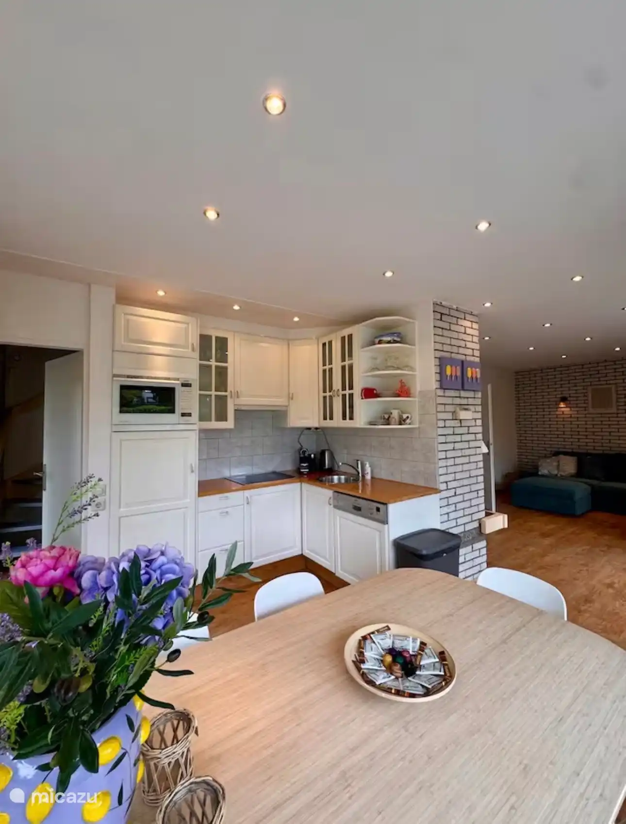 Open leefruimte waar keuken, eetkamer en woonkamer naadloos samenkomen. Lichte kleuren, warme houtaccenten en sfeervolle verlichting creëren een gezellige en uitnodigende sfeer.