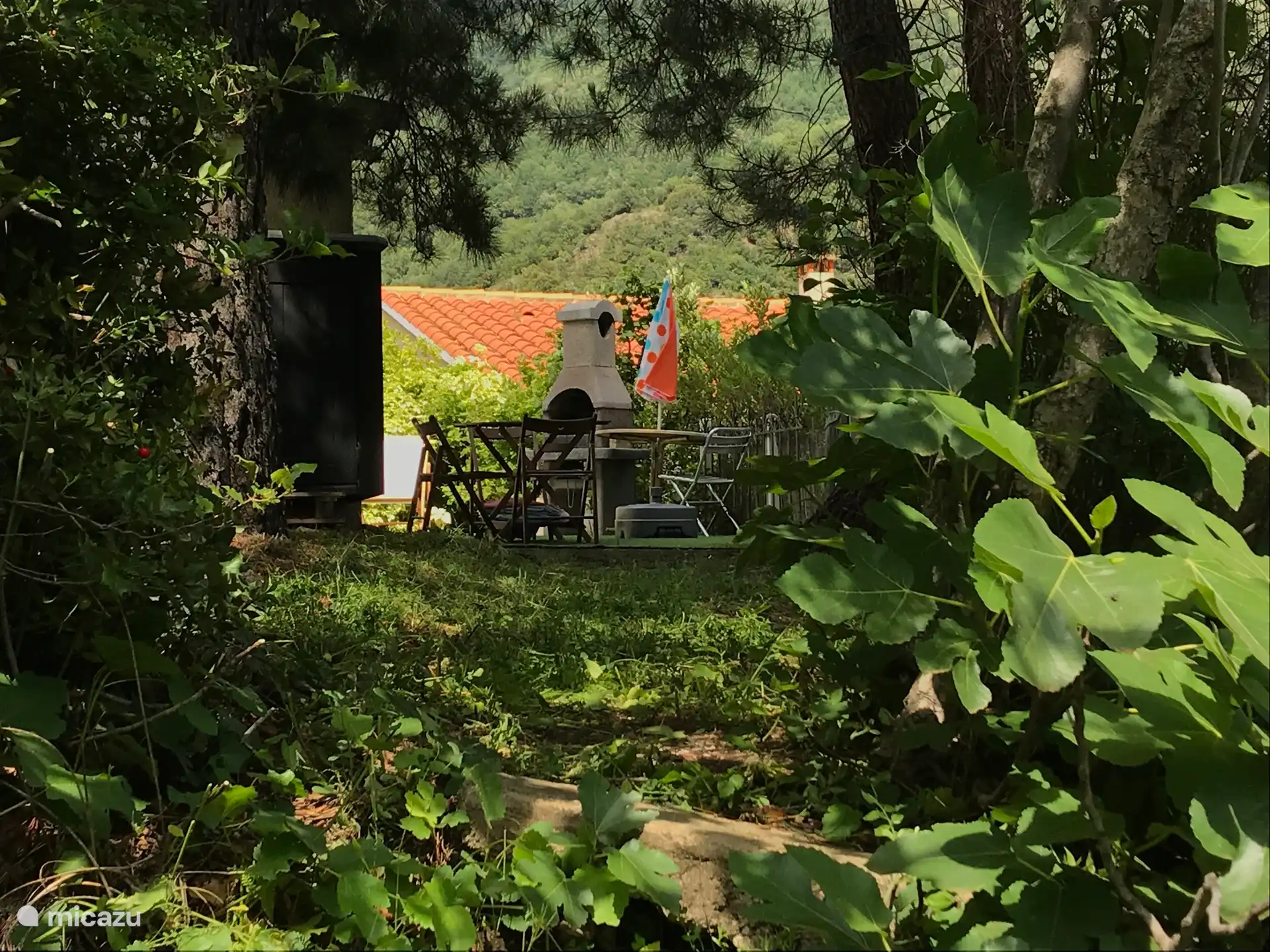 Jardín con gran mesa, barbacoa y parsol