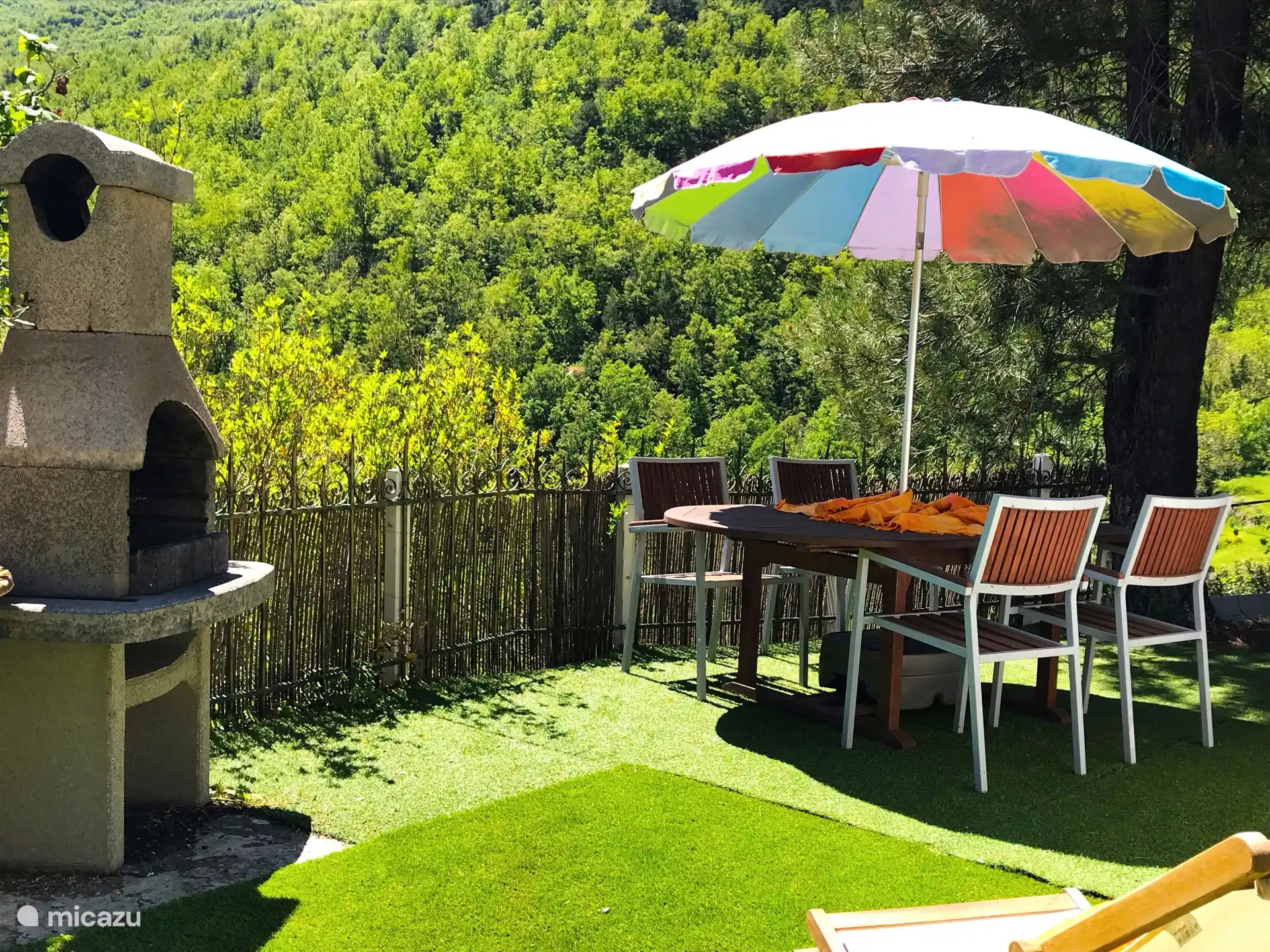 Jardín con gran mesa, barbacoa y parsol
