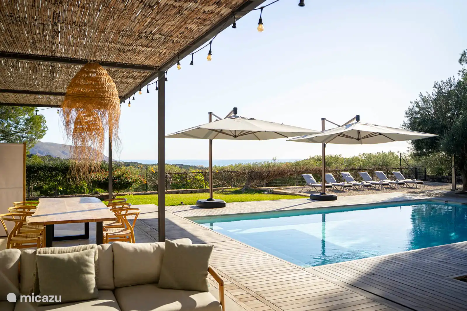 Zwembad omringd door een terras met ligstoelen, een tuin met bomen, uitzicht op natuur en zee, en een buitenlounge.