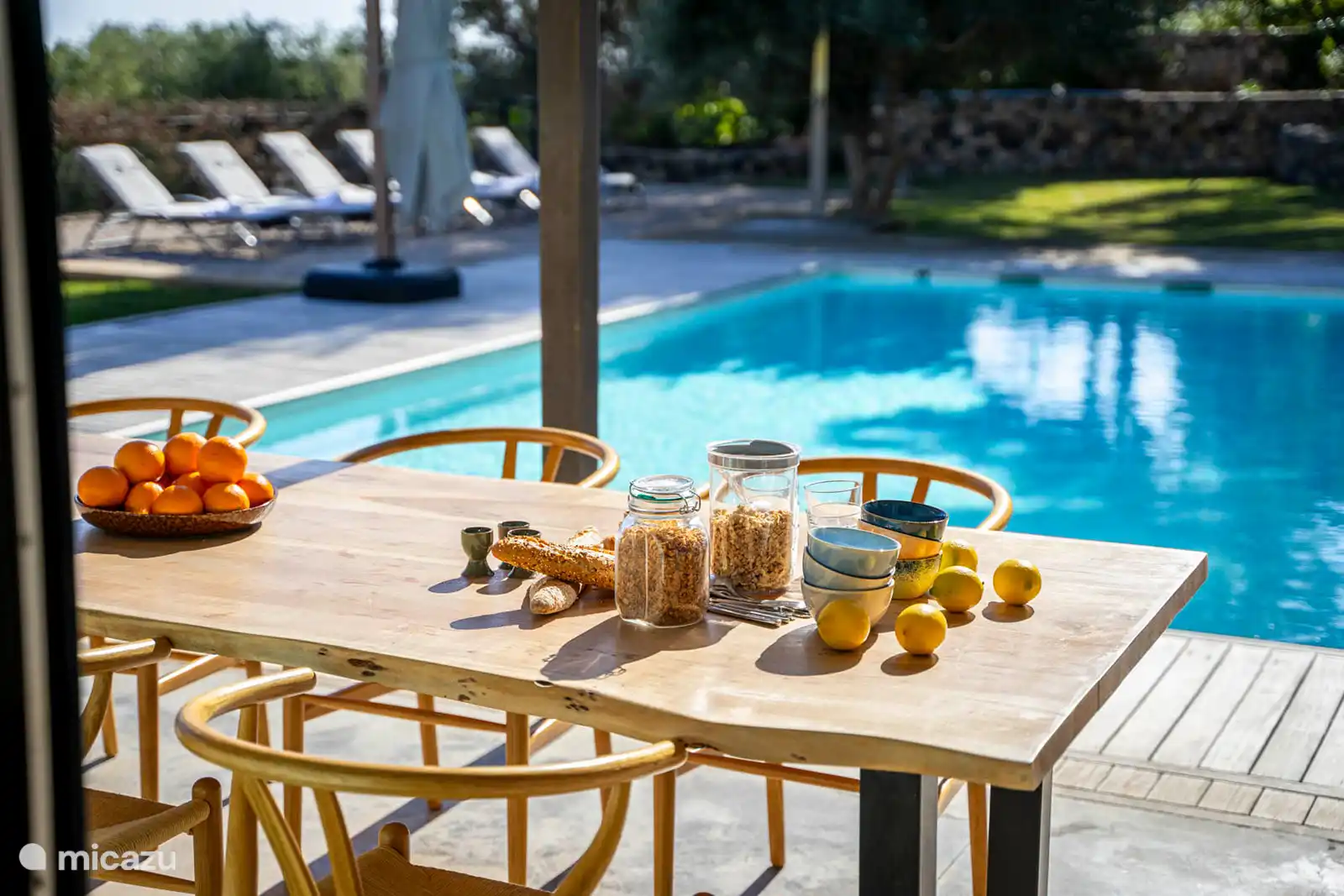 Zwembad omringd door een terras met ligstoelen, een tuin met bomen, uitzicht op natuur en zee, en een buitenlounge.
