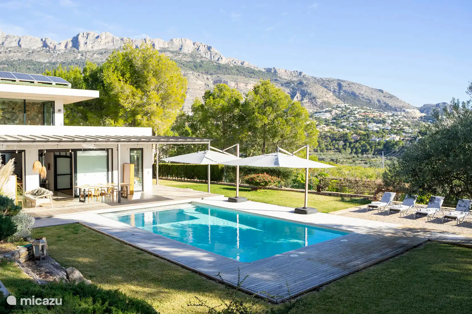 Zwembad omringd door een terras met ligstoelen, een tuin met bomen, uitzicht op natuur en zee, en een buitenlounge.