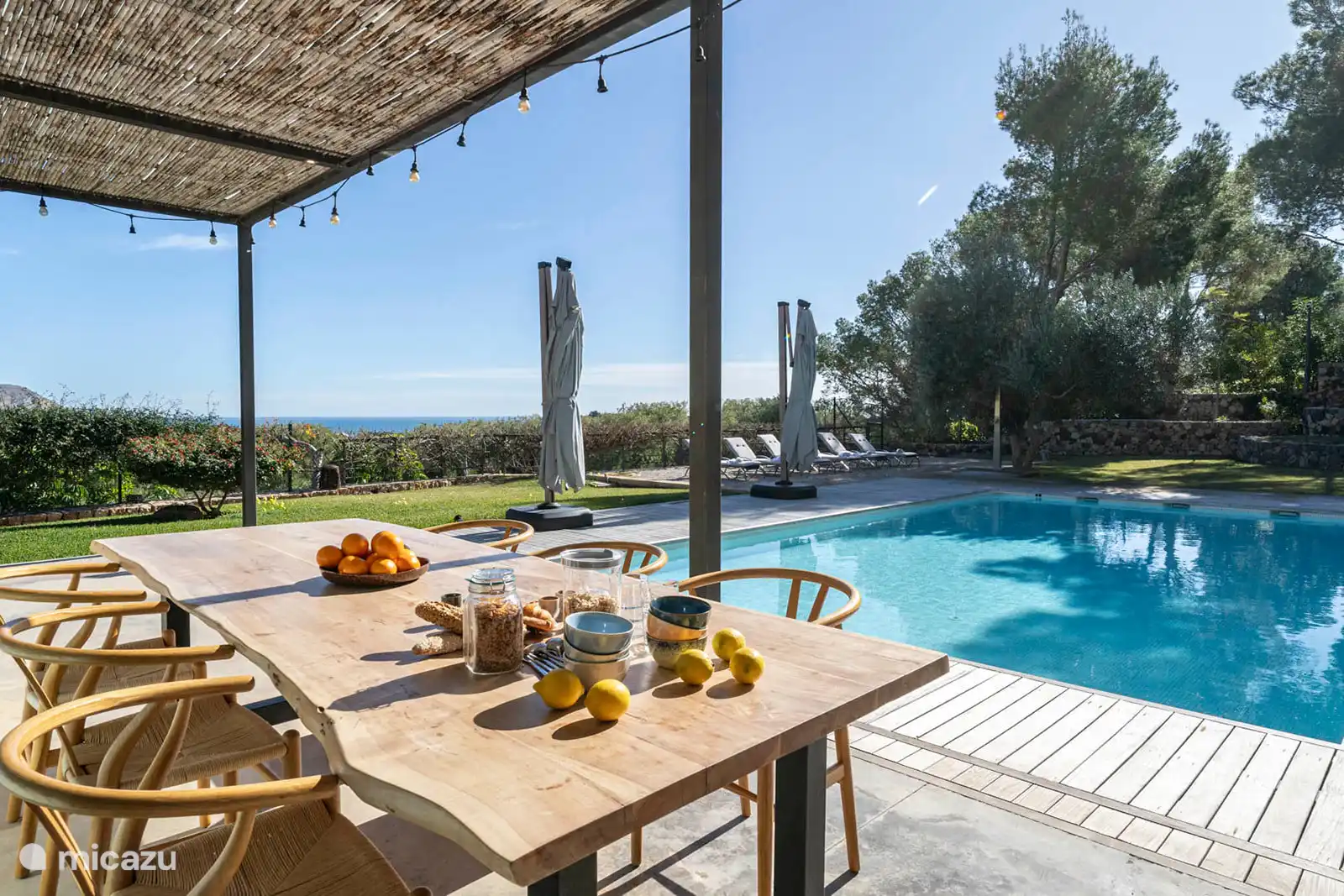 Zwembad omringd door een terras met ligstoelen, een tuin met bomen, uitzicht op natuur en zee, en een buitenlounge.