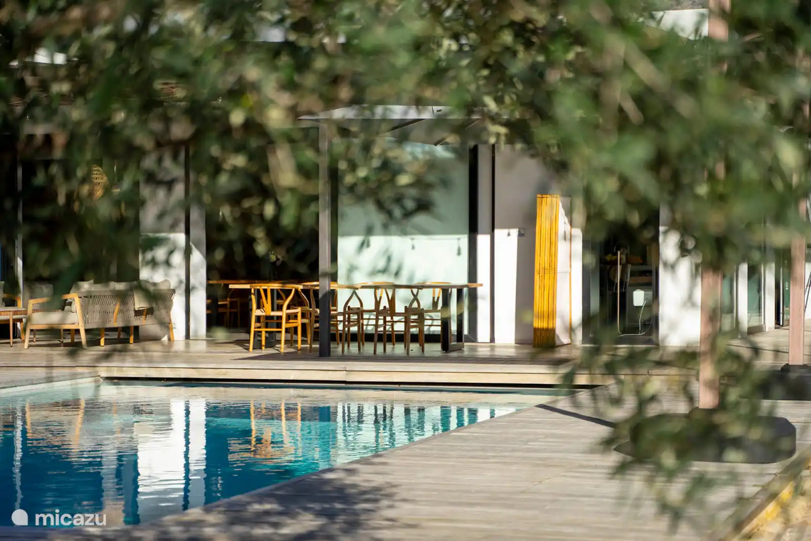 Zwembad omringd door een terras met ligstoelen, een tuin met bomen, uitzicht op natuur en zee, en een buitenlounge.