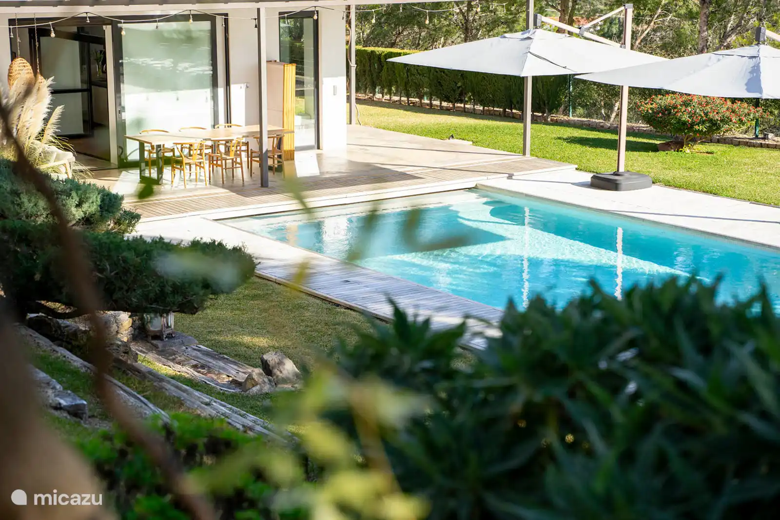 Zwembad omringd door een terras met ligstoelen, een tuin met bomen, uitzicht op natuur en zee, en een buitenlounge.