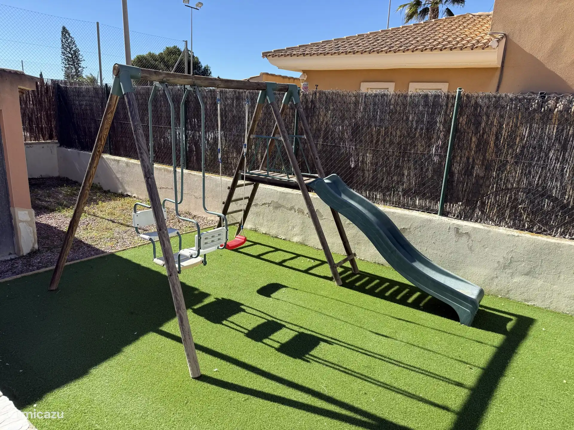 In de achtertuin is een speeltoestel met schommel en glijbaan aanwezig
