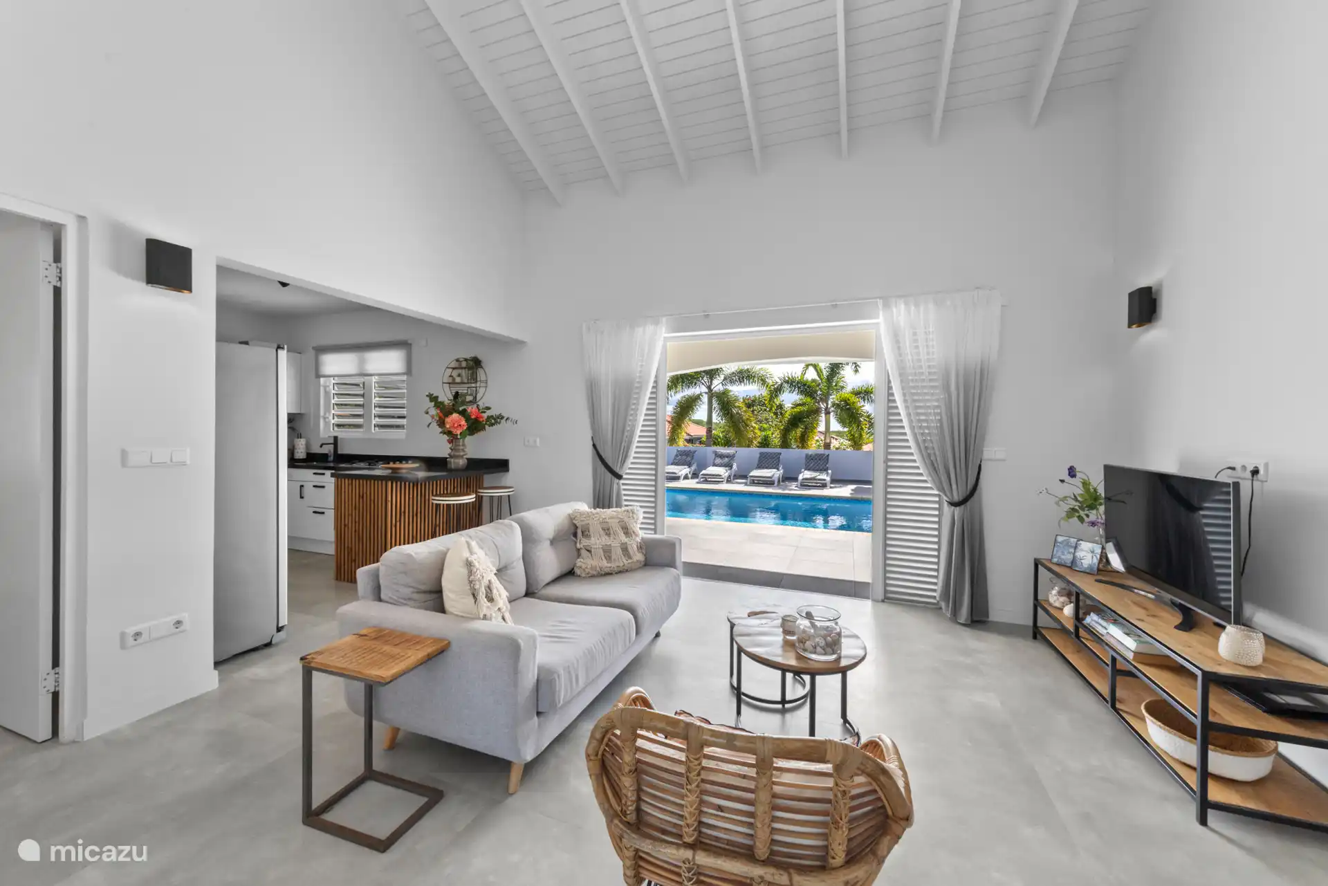 Compleet ingerichte woonkamer met open keuken en zicht op de buitenruimte met de openslaande deuren. 