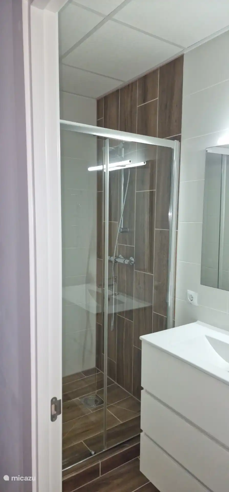 Badkamer kleine slaapkamer appartement met douche, wastafelmeubel met handdoeken en een toilet. Shampoo, conditioner en douchegel  en toiletpapier aanwezig.