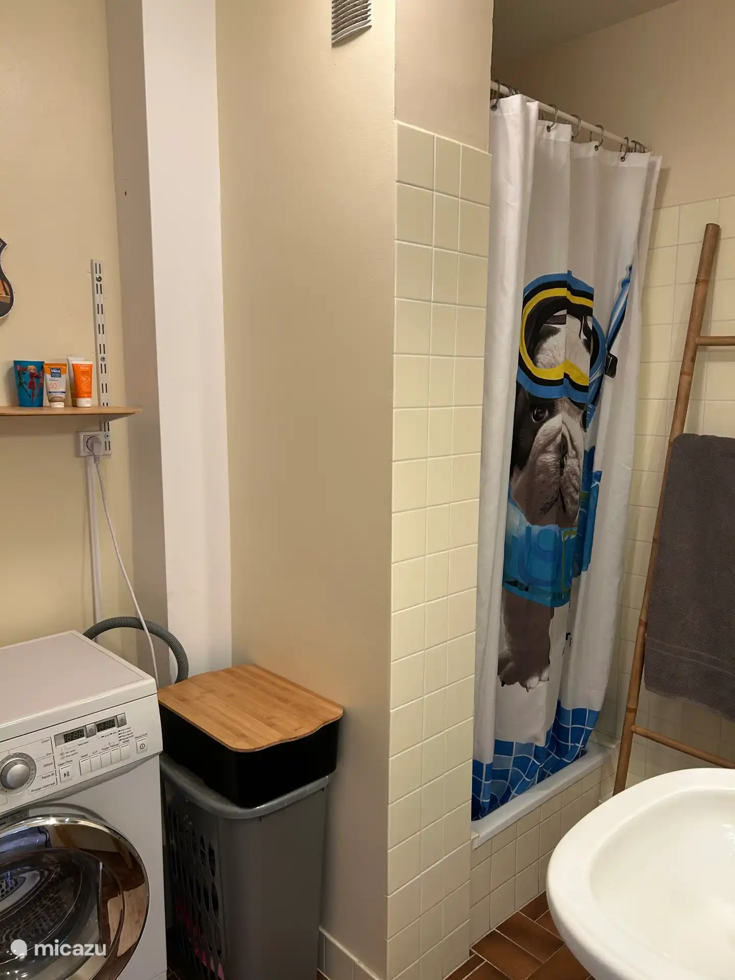 Salle de bain avec douche, lavabo, machine à laver et meuble de rangement.