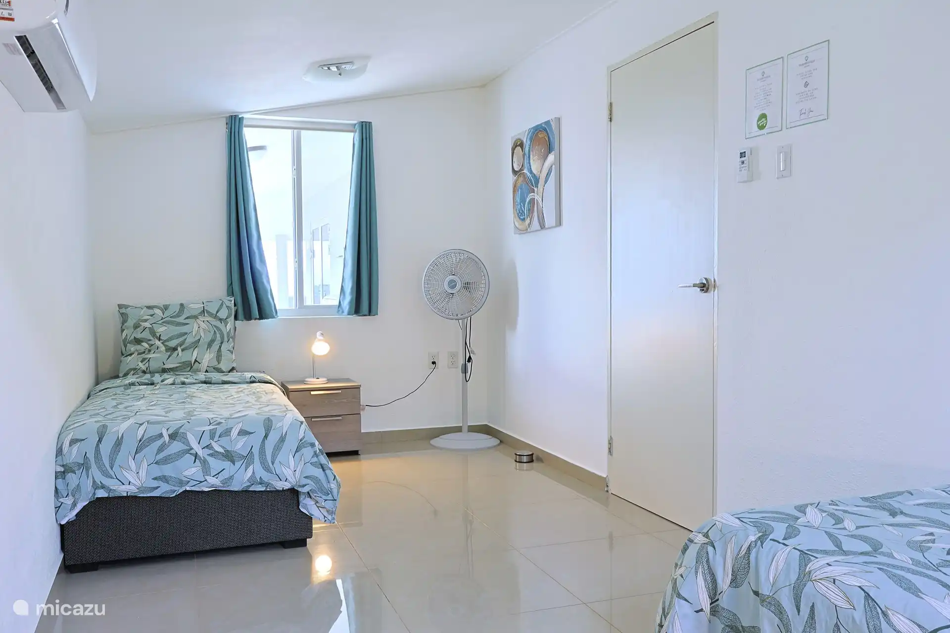 Slaapkamer met twee eenpersoons bedden, airconditioning, opbergruimte en fan.