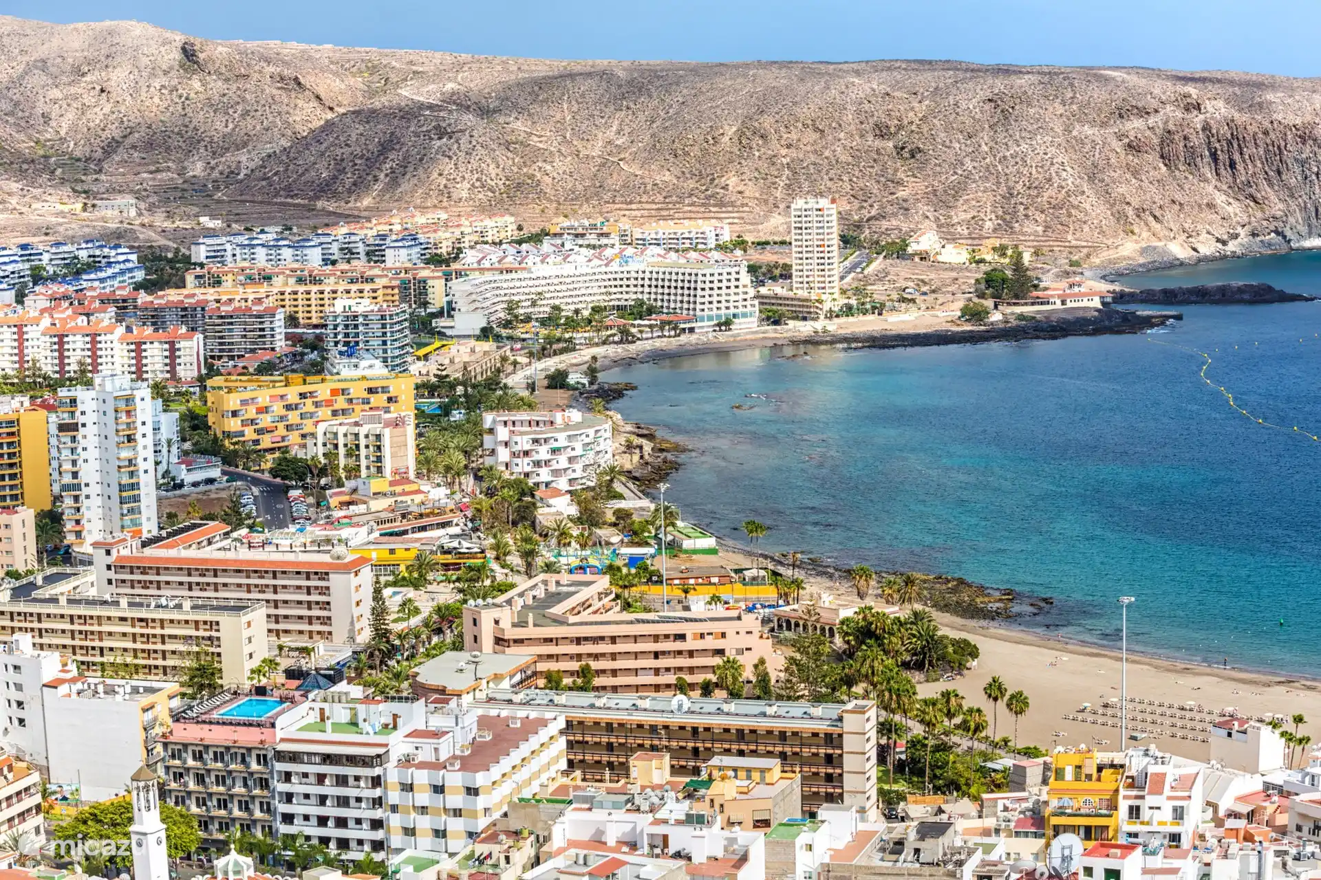 Uitzicht over Los Cristianos met de kustlijn, het strand en de omliggende bergen. Een levendige omgeving waar stad, zee en natuur samenkomen.