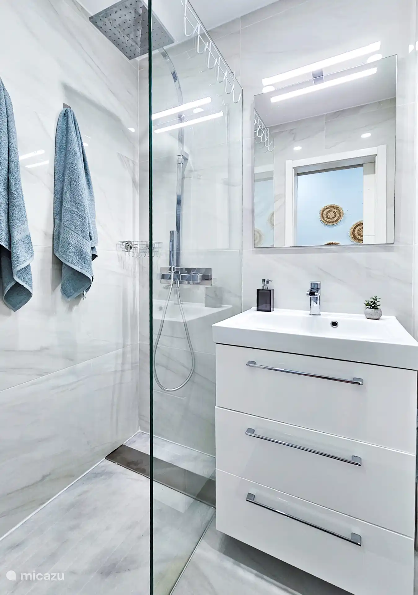 Moderne badkamer met marmeren accenten en een ruime inloop-regendouche. Voorzien van elegant wastafelmeubel en opbergruimte. 