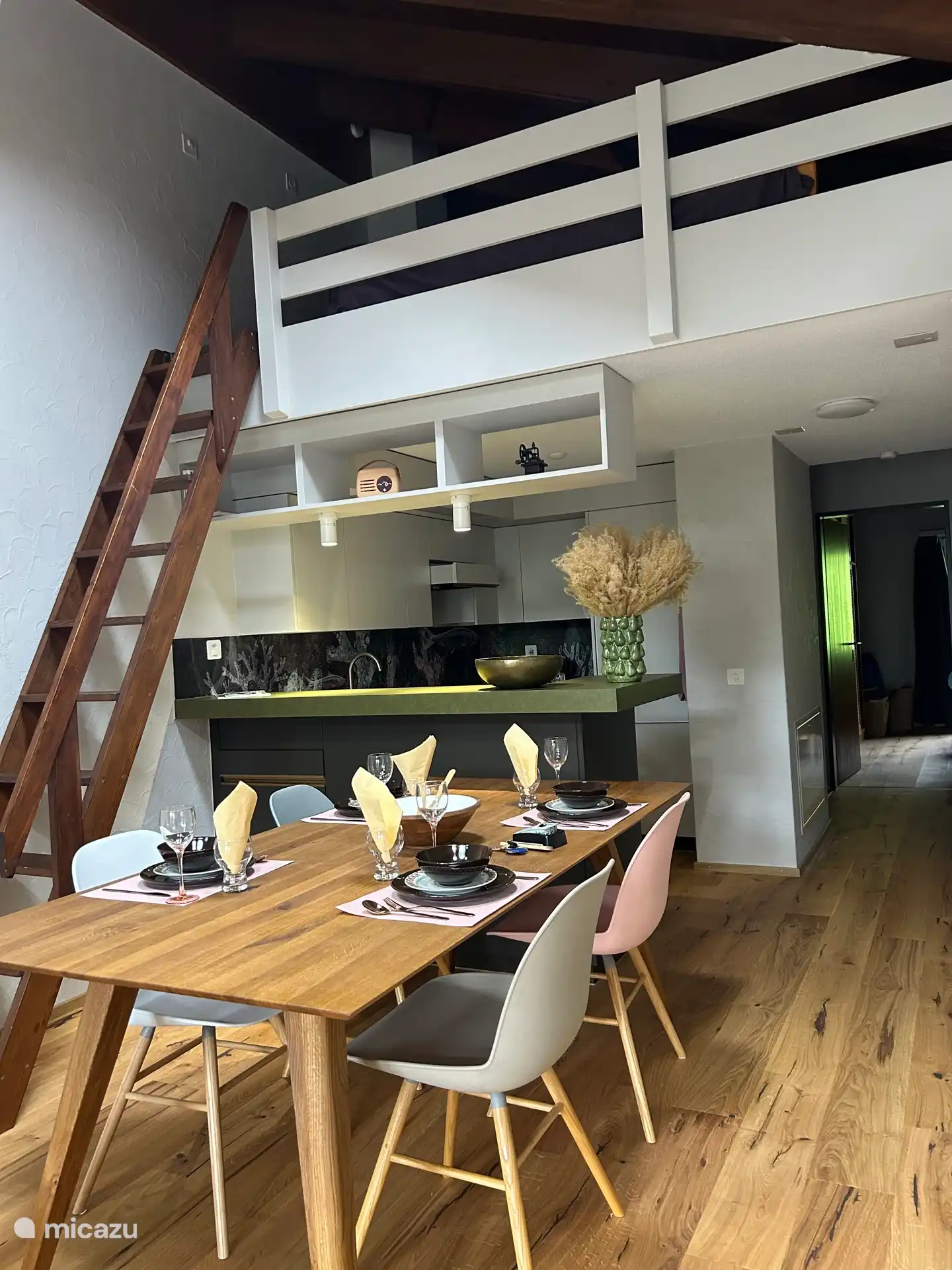 Fotografiado desde el lado del balcón. Aquí se ve la espaciosa mesa del comedor con la cocina abierta detrás. Las escaleras conducen a la galería con una cama matrimonial.