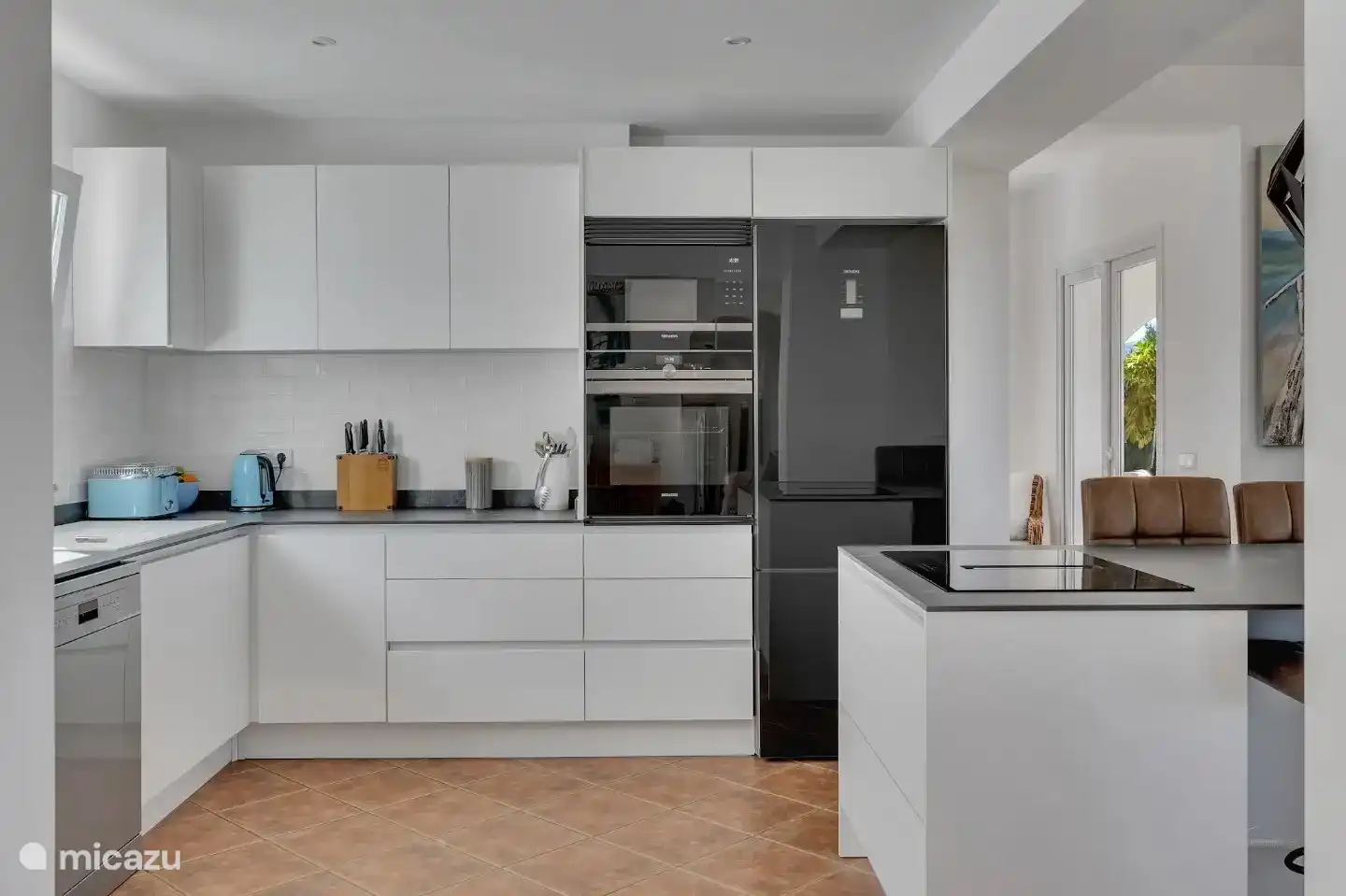 La cocina de planta abierta tiene electrodomésticos Seimens de cristal negro de gama alta y una gran isla. 