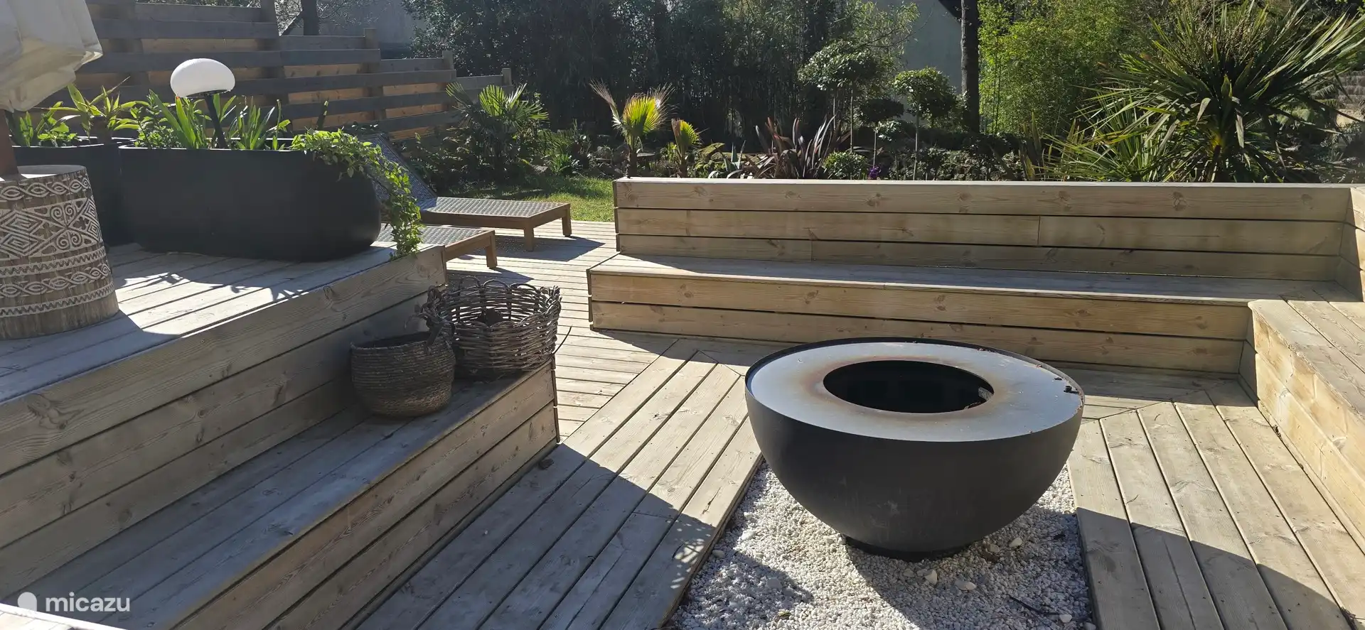 Espace extérieur aménagé avec terrasse en bois, brasero central et coins détente, idéal pour partager des moments conviviaux en plein air dans un cadre végétalisé et apaisant.