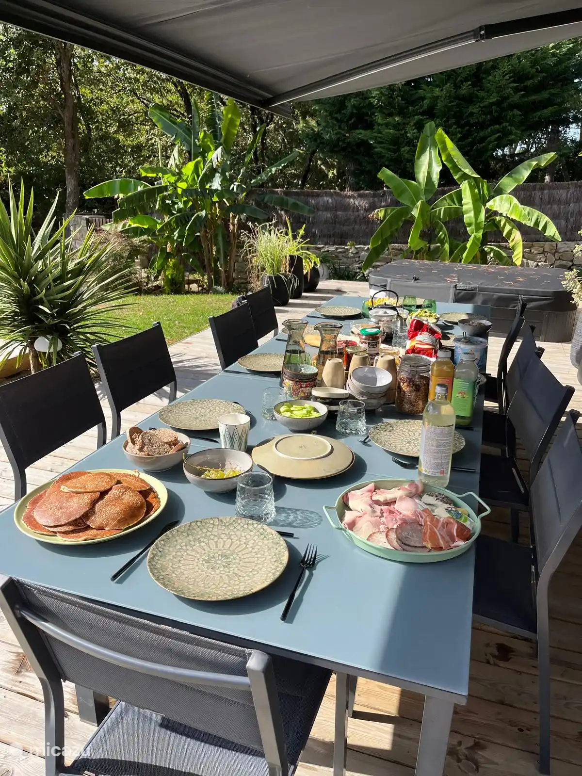 Grande table extérieure sous store banne, idéale pour partager des repas en plein air à l’ombre, dans un cadre convivial et verdoyant.