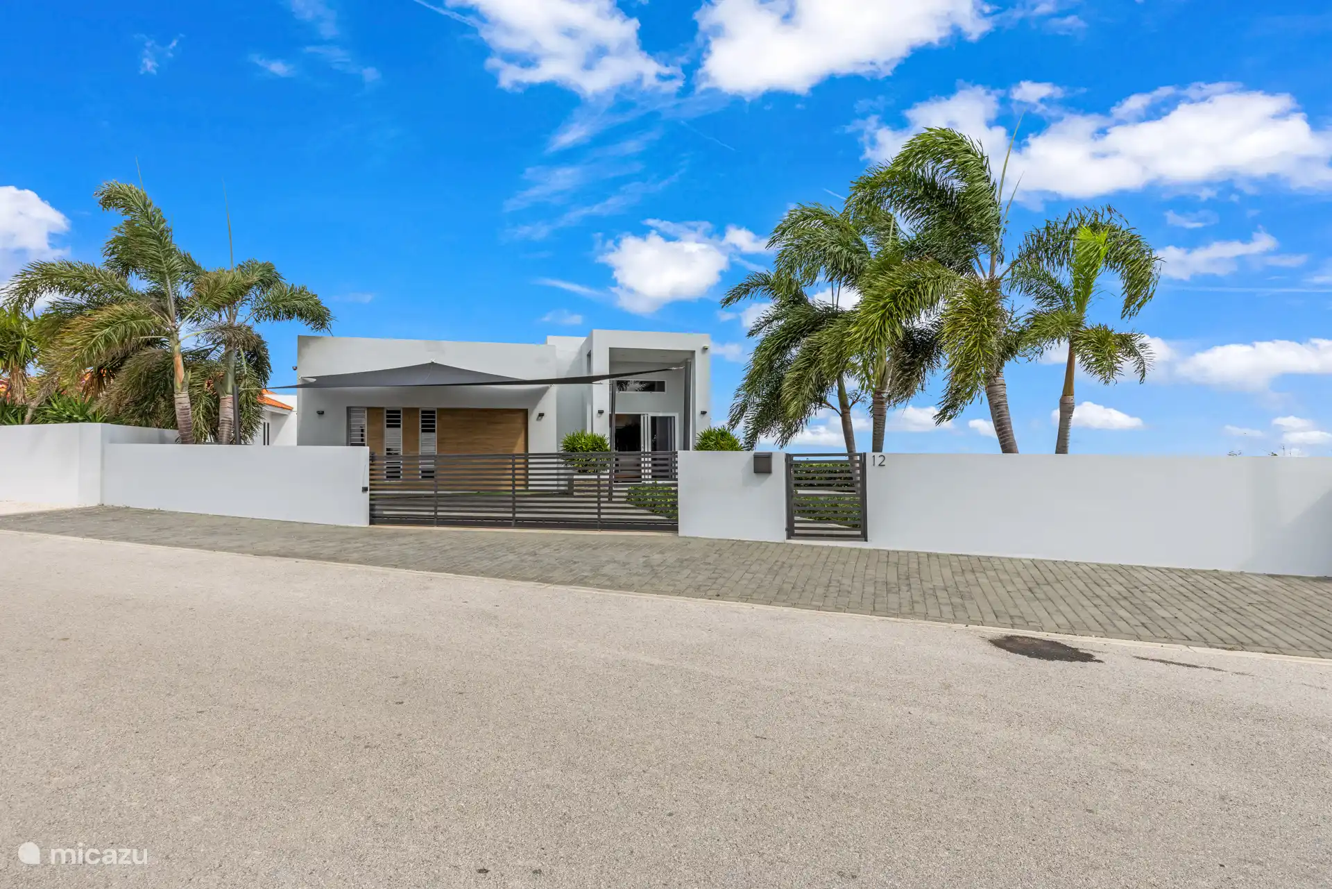 Overzicht van de villa met afgesloten terrein, elektrisch hek en parkeerruimte met schaduwdoek