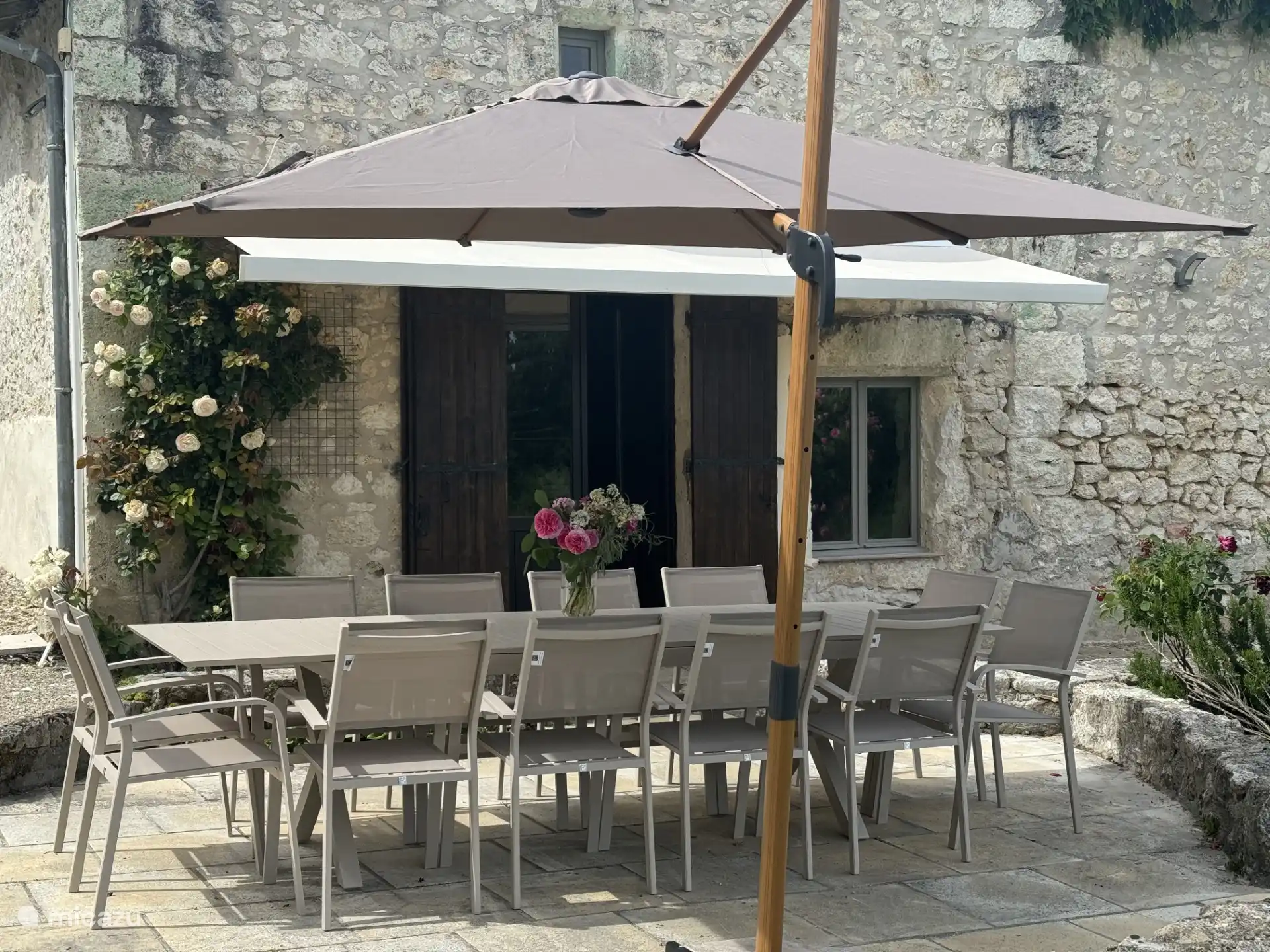 Terraza en la parte delantera de la casa con mesa de comedor, parasol, barbacoa y vistas al jardín y al campo circundante.